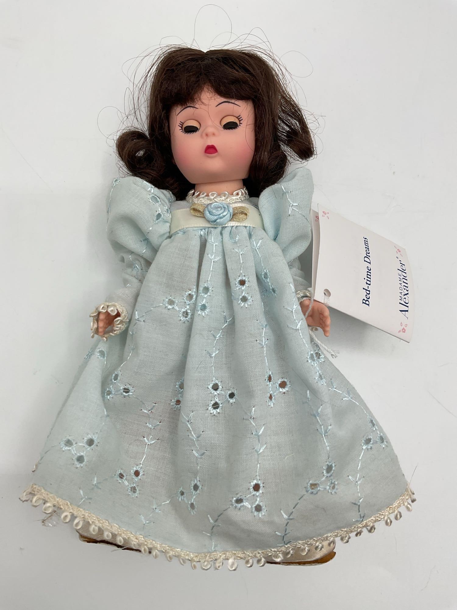 Vintage Porcelain Doll- Bedtime Dreams, Madame Alexander: A small porcelain collectible doll with dark brown hair styled in ringlets, wearing a powder blue dress with delicate eyelet embroidery and lace trim. The doll has hand-painted facial features and por