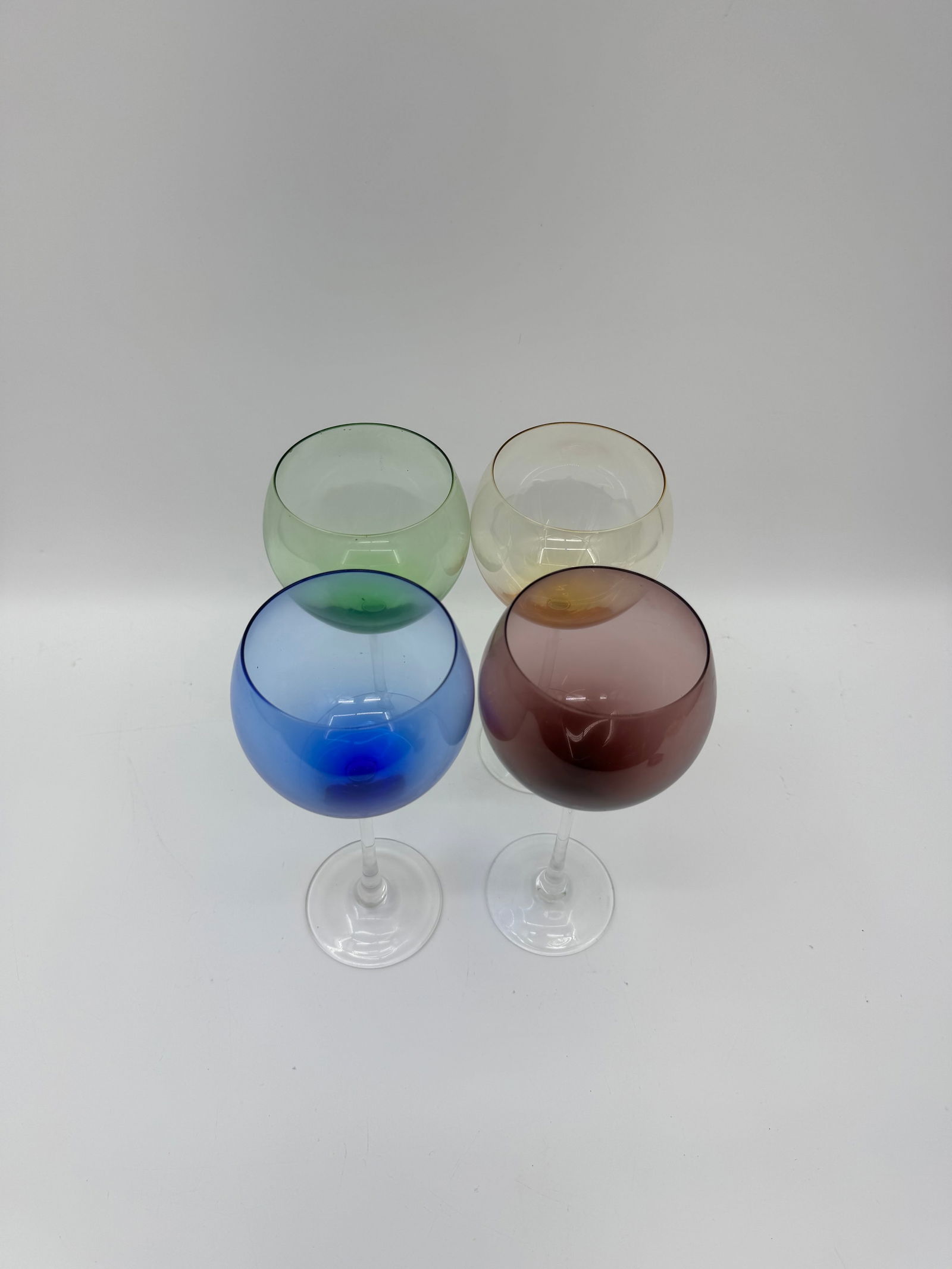 Set of 4 Mid-Century Colored Glass Goblets: Vibrant set of four mid-century goblets in assorted colors—blue, amber, green, and plum. Each glass features a clear stem and rounded bowl, adding a playful yet elegant touch to any table settin
