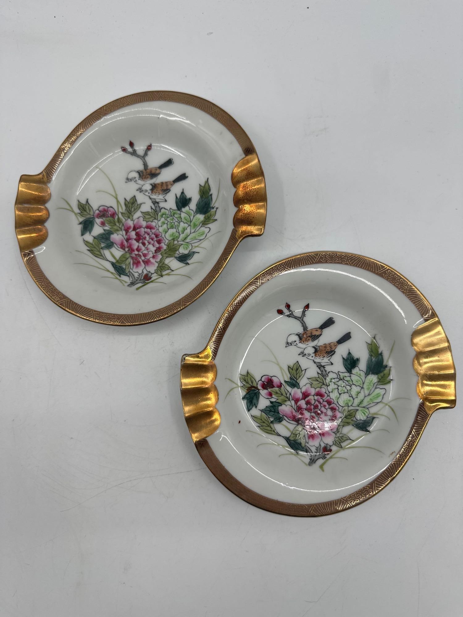 Pair of Kutani Porcelain Ashtrays with Floral Motif and Gold Handles: Set of two hand-painted white porcelain ashtrays featuring hand-painted floral designs and gold-tone handles. Dimensions: H:1in L:6in W:6in