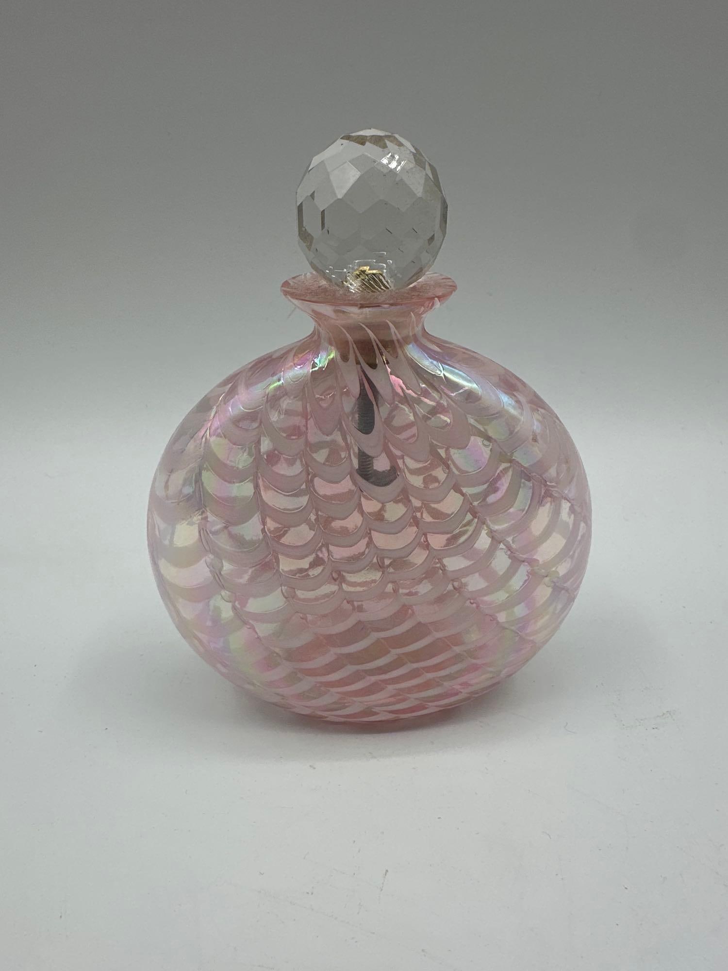 Iridescent Pink Art Glass Perfume Bottle with Faceted Stopper: Round iridescent pink art glass perfume bottle featuring a decorative scale-like swirl pattern. Topped with a faceted crystal stopper set in brass, which appears to be mounted on a threaded rod, possi