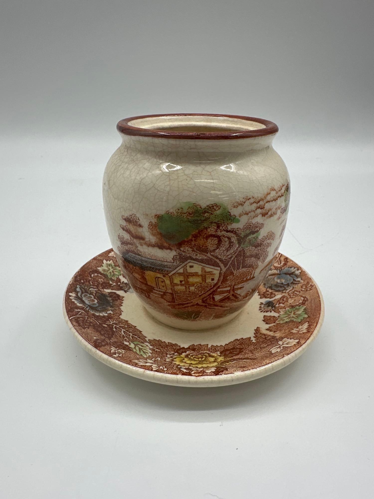 Nasco Mountain Woodland Ceramic Planter and Saucer: Vintage ceramic planter with matching saucer from the "Mountain Woodland" series by Nasco. Features a rustic landscape scene with a cottage and floral border, accented by intentional crazing