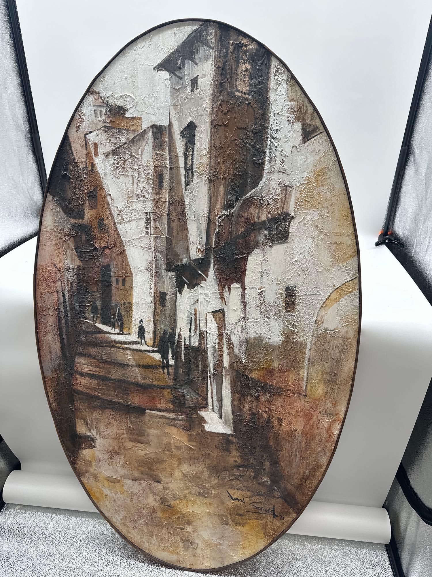 Mediterranean Alleyway by Jonas Gerard (American, b.1941) Oil on canvas: Oval-shaped textured painting of a narrow Mediterranean street with tall, sunlit buildings and distant figures in shadow. The artist uses a palette of earthy browns, whites, and ochres with heavy text