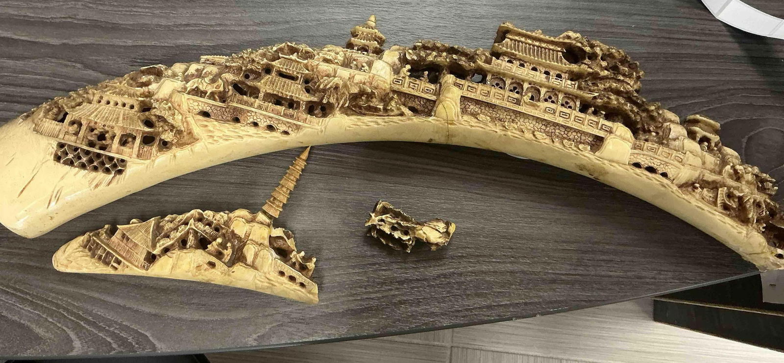Chinese Village Landscape Carving on Faux Ivory: Intricately carved curved sculpture depicting a detailed village scene with pagodas and traditional architecture. Likely made of resin imitating ivory. Shows breakage with two detached sections.Medium