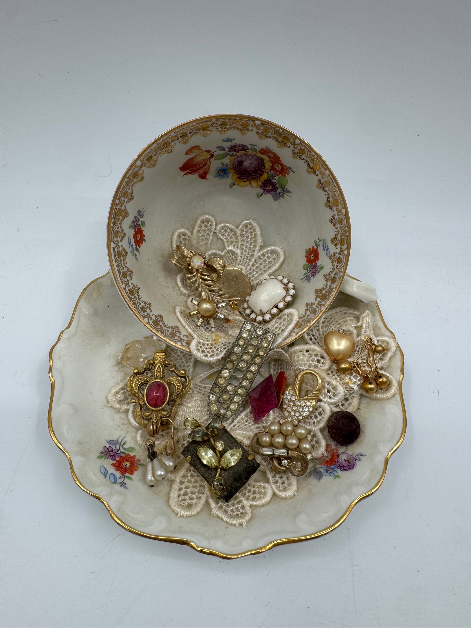 Vintage Schumann US Zone Teacup and Saucer with Jewelry: Vintage Schumann US Zone teacup and saucer featuring floral decoration, repurposed as a jewelry holder. Includes an assortment of vintage brooches and pins. Teacup measures approximately 6 inches wide