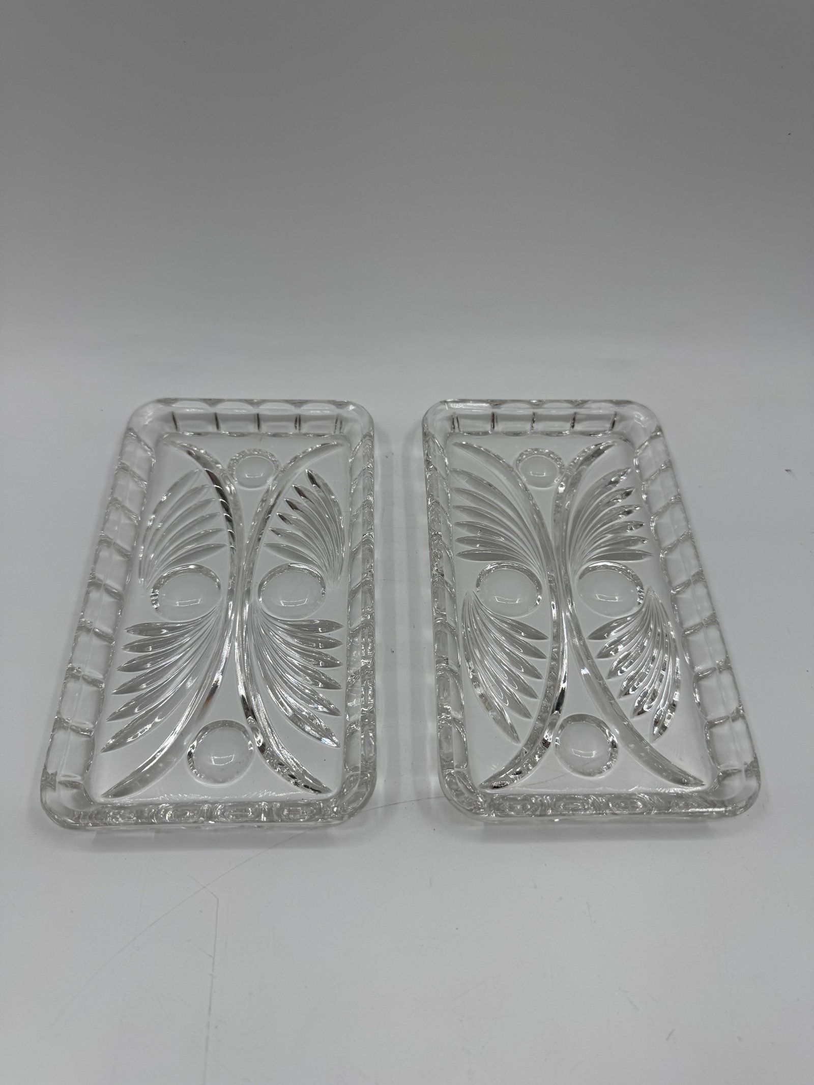 Pair of Clear Glass Dresser Trays: Pair of clear glass dresser trays, each with a rectangular shape and decorative molded design. Approximate dimensions: 7 x 4 inches.