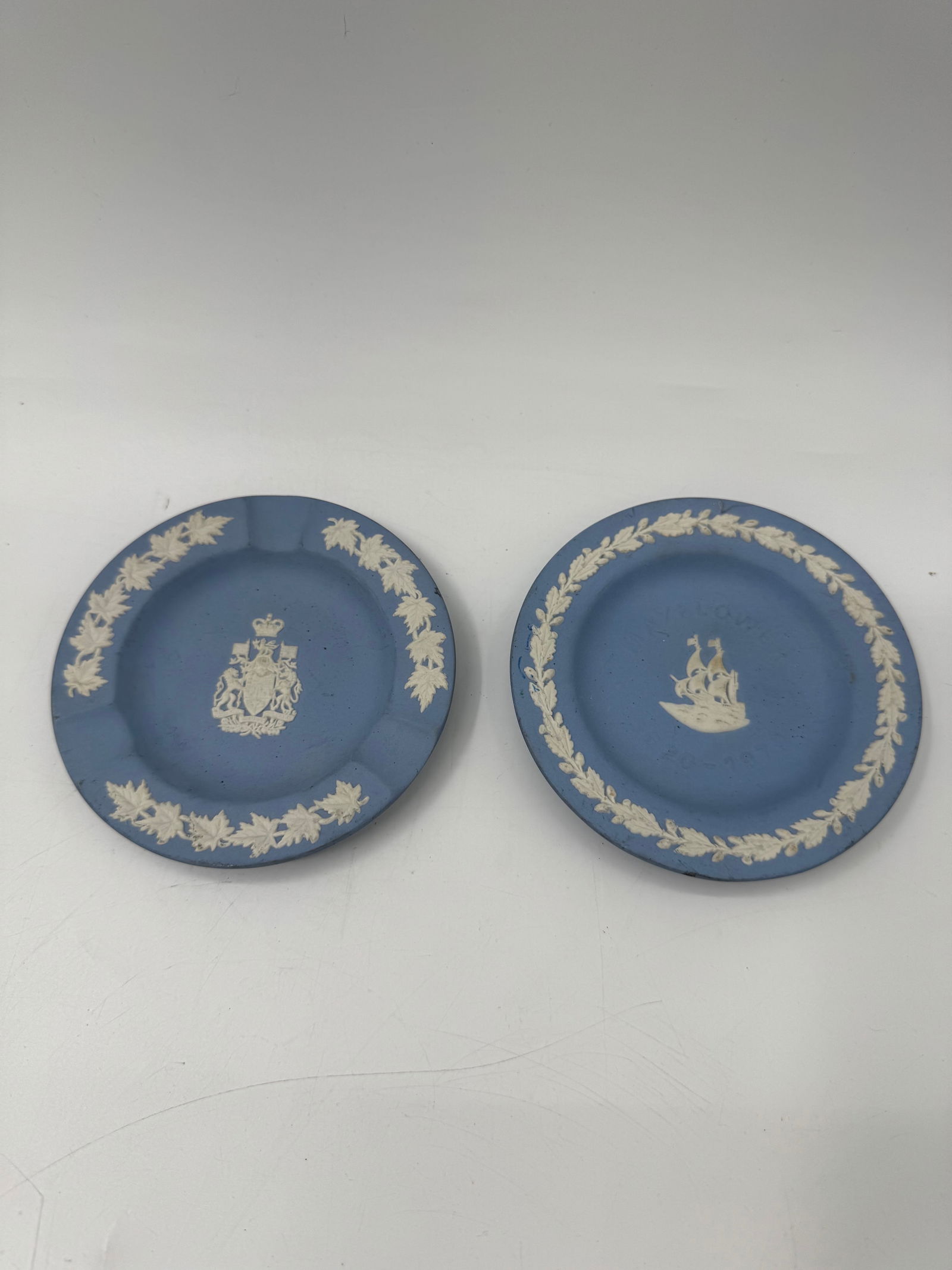 Pair of Wedgwood Jasperware Plates, Canada Coat of Arms: Pair of Wedgwood light blue jasperware plates. One plate features the Coat of Arms of Canada, and the other depicts a sailing ship. Both plates have a floral border. Each plate is approximately 4.5 in