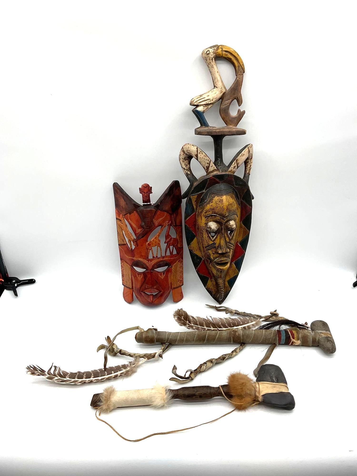 African Tribal Masks and Ceremonial Tools Collection: Group of hand-carved African tribal items including two stylized masks with geometric and figurative detailing, and three traditional ceremonial tools with stone heads, feathers, fur, and leather acce