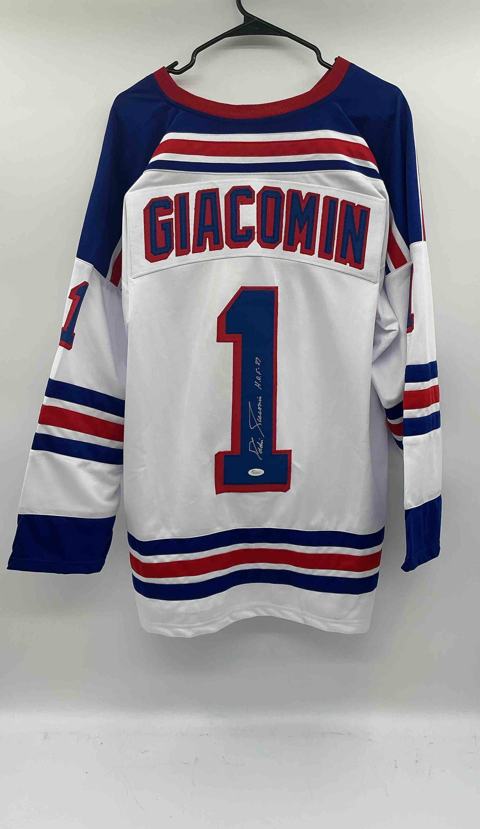 Ed Giacomin Autographed New York Rangers Jersey:  White New York Rangers jersey with number 1, signed by Ed Giacomin with HOF inscriptionMedium: Fabric with stitched lettering and ink signature