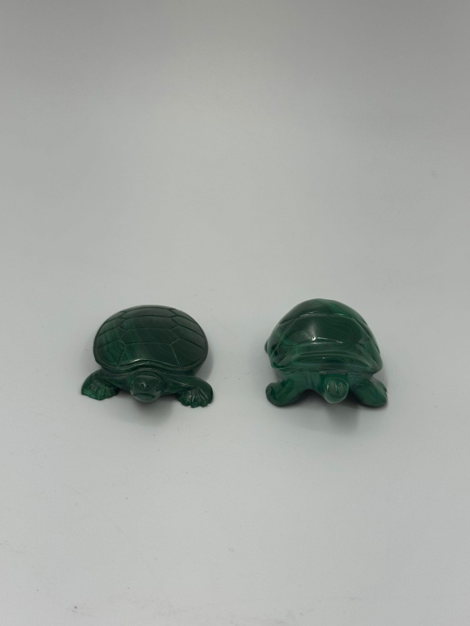 Two Carved Malachite Turtle Figurines: Two small, carved turtle figurines made of malachite. Each turtle has a detailed shell and is approximately 1.5 inches long. The carvings are simple yet elegant, showcasing the natural banding of the
