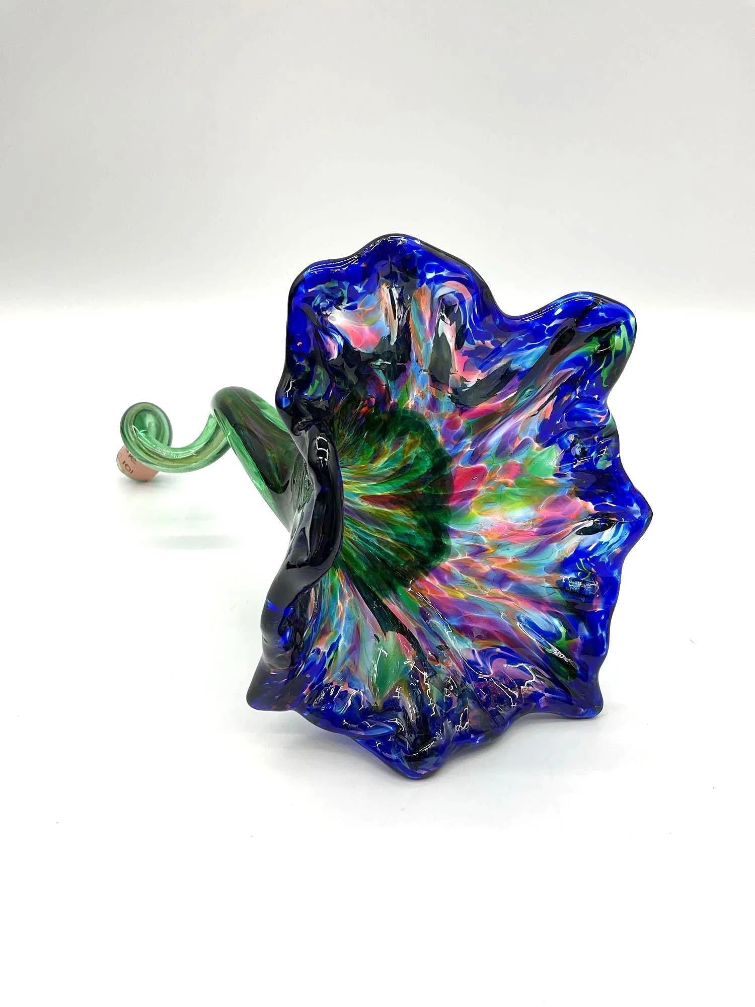 Hand-Blown Art Glass Trumpet Flower Sculpture:  Vibrant hand-blown glass sculpture shaped like a trumpet flower, featuring an iridescent ruffled bloom in deep blue and multicolor tones with a twisted green stem. Dimensions: H10in L6in W5in M