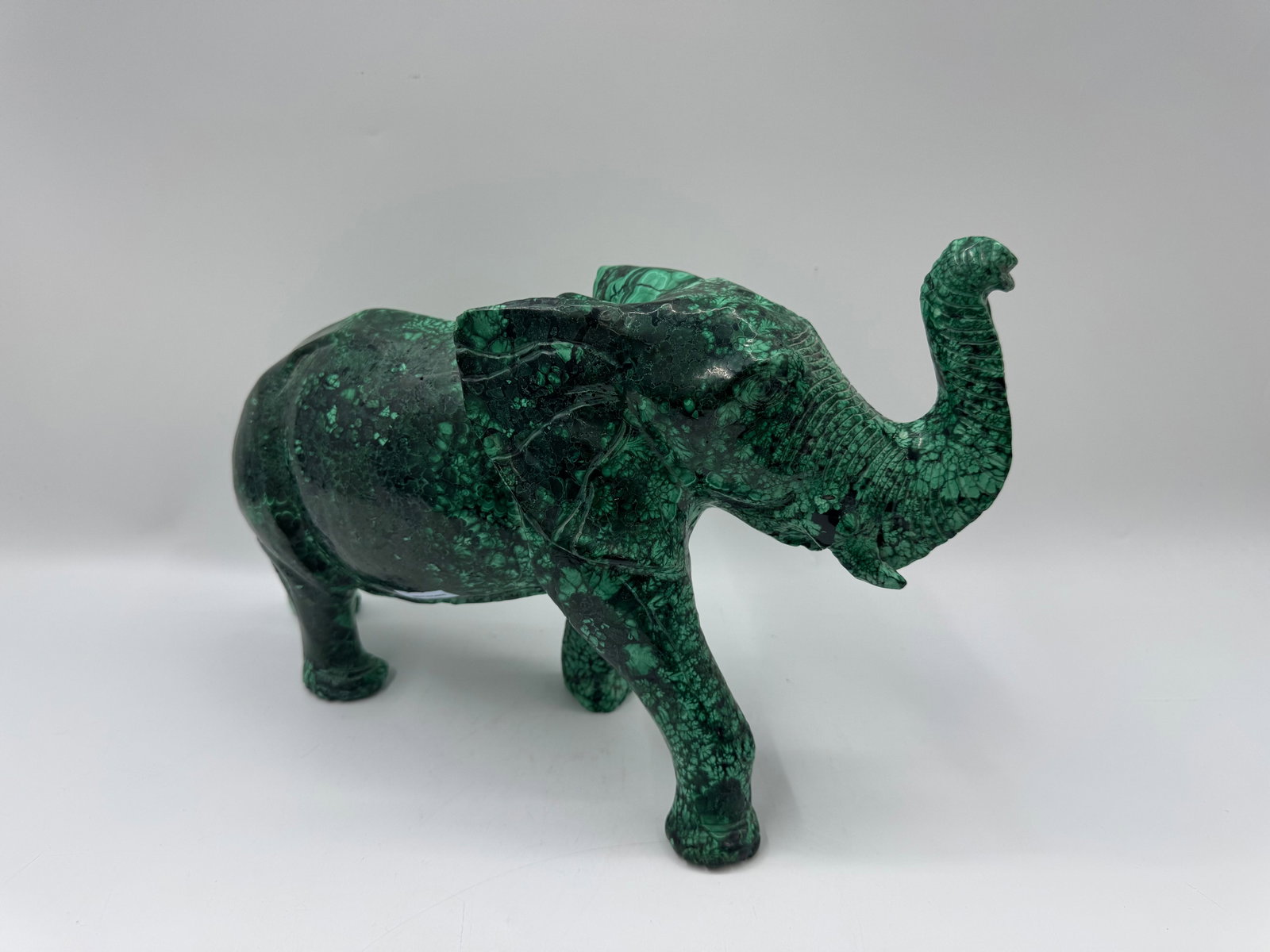 Malachite Elephant Sculpture: A malachite elephant sculpture, measuring approximately 13x10x5 inches. The piece features a rich green color with natural banding patterns characteristic of malachite. A decorative and eye-catching p
