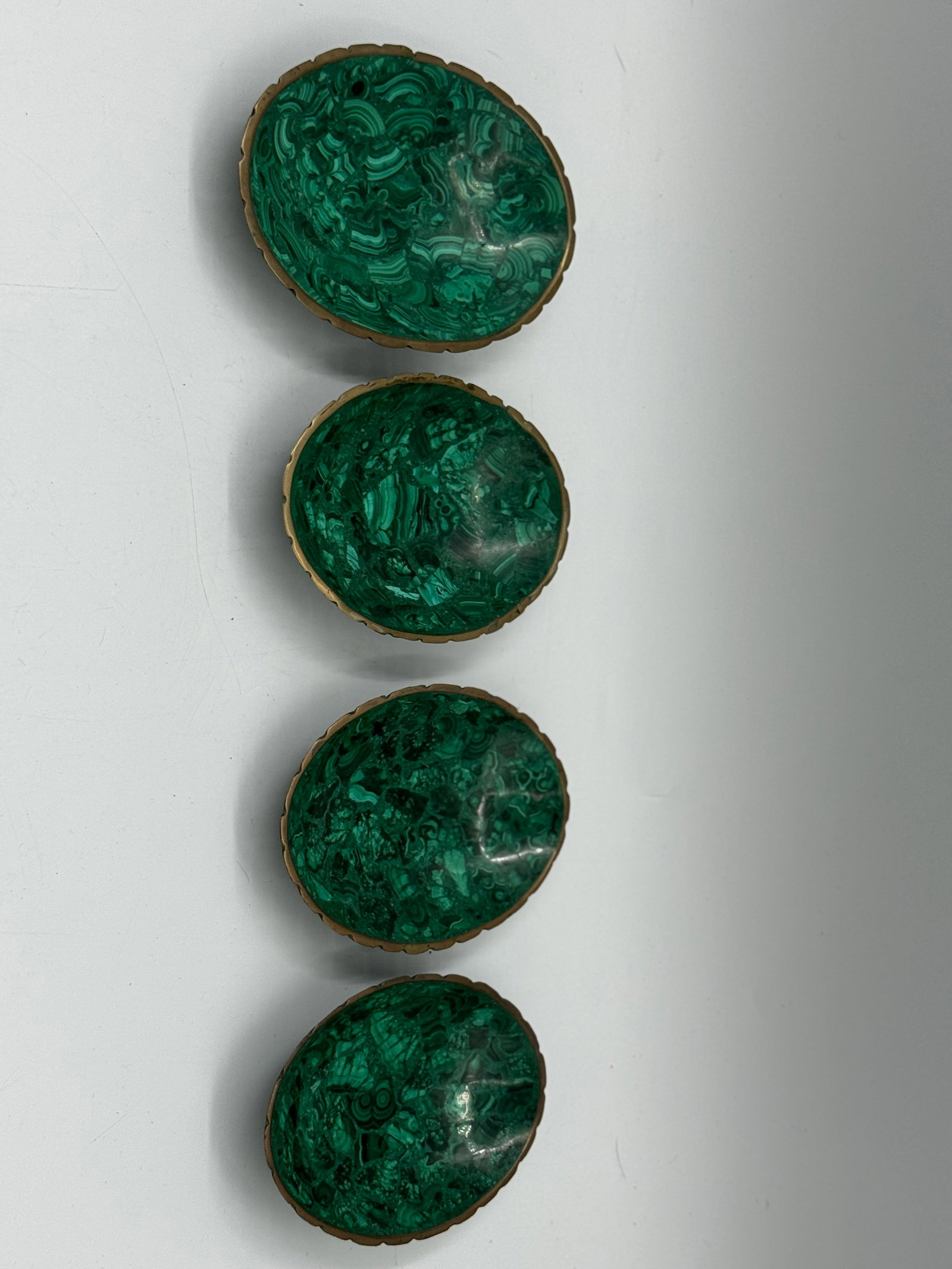 Set of Four Malachite Cabochons in Metal Bezels: Set of four oval malachite cabochons, each set in a decorative metal bezel. The stones exhibit characteristic banding and rich green hues. 6x4.5in