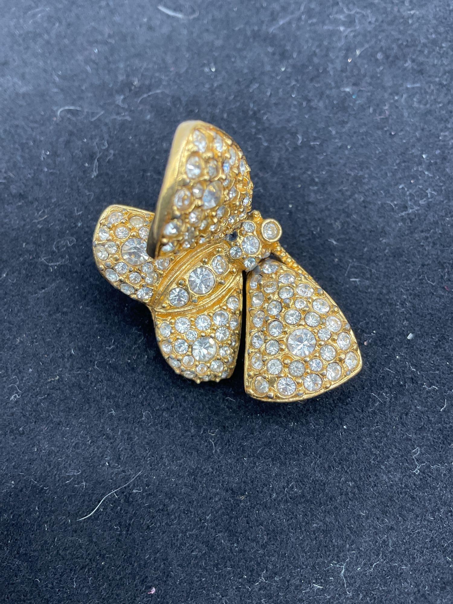 KJL by Kenneth Jay Lane Pave Crystal Bow Brooch: Elegant gold-tone brooch in the shape of a bow, encrusted with sparkling pave-set rhinestones. Signed KJL on the reverse. Dimensions: L1in Medium: Gold-tone metal and rhinestones