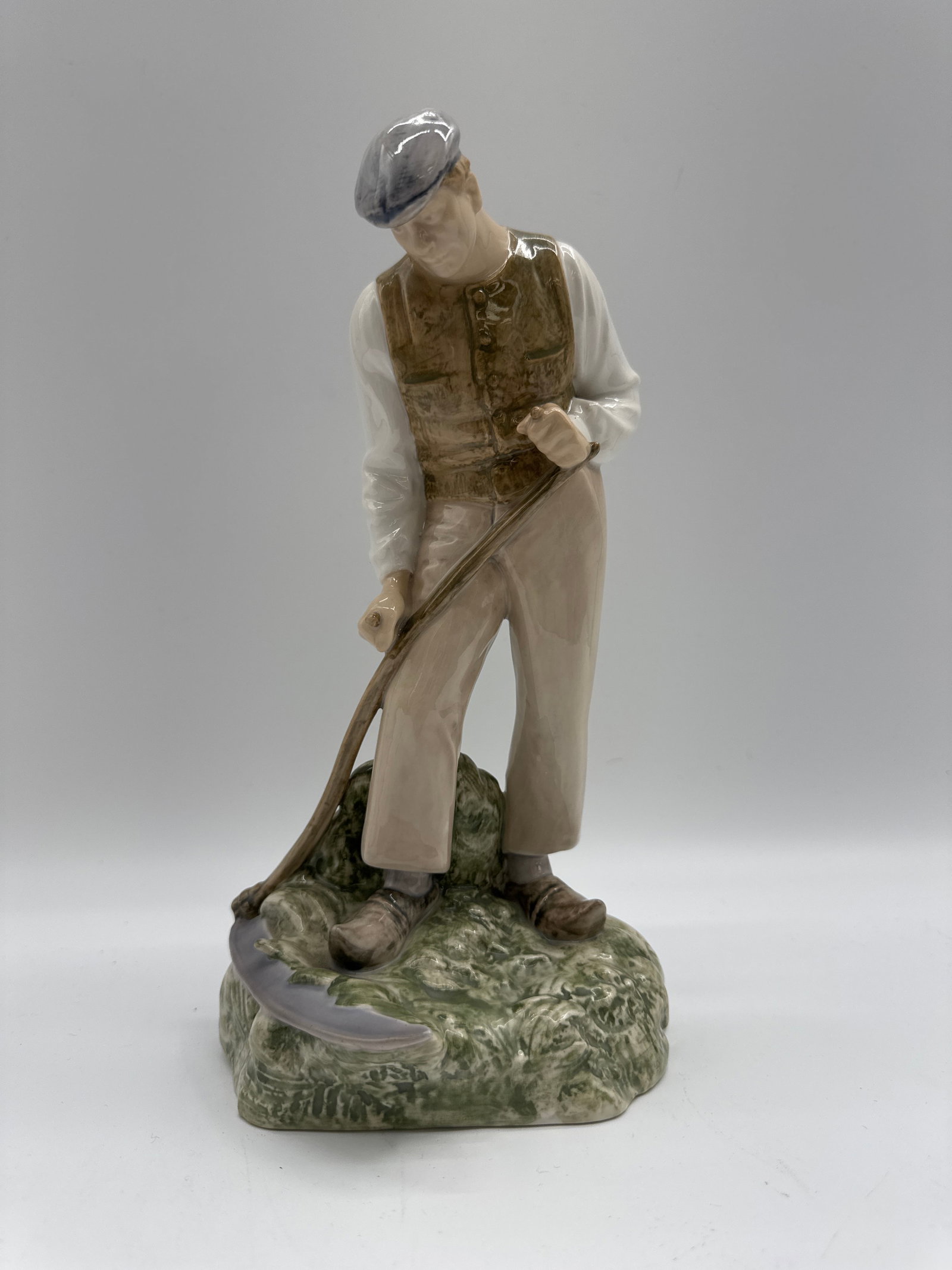 Bing Grondahl Harvest Man with Scythe: Porcelain figurine depicting a man with a scythe. Marked on the bottom. Measures approximately 9 inches tall.