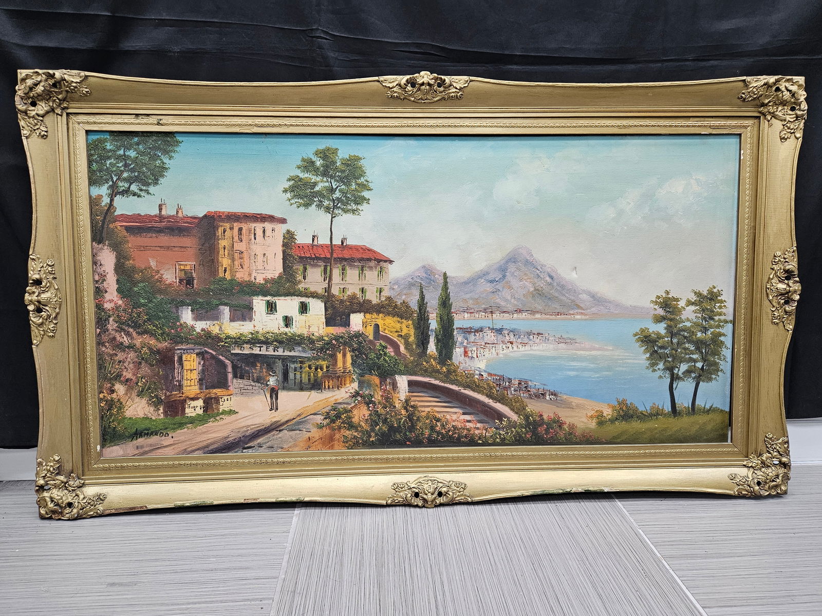 Coastal Italian Village by Armando Oil on Canvas: Description: Oil on canvas painting depicting a coastal Italian village scene, signed 'Armando' lower left. Presented in an ornate gilt frame. The painting features buildings on a hillside ove