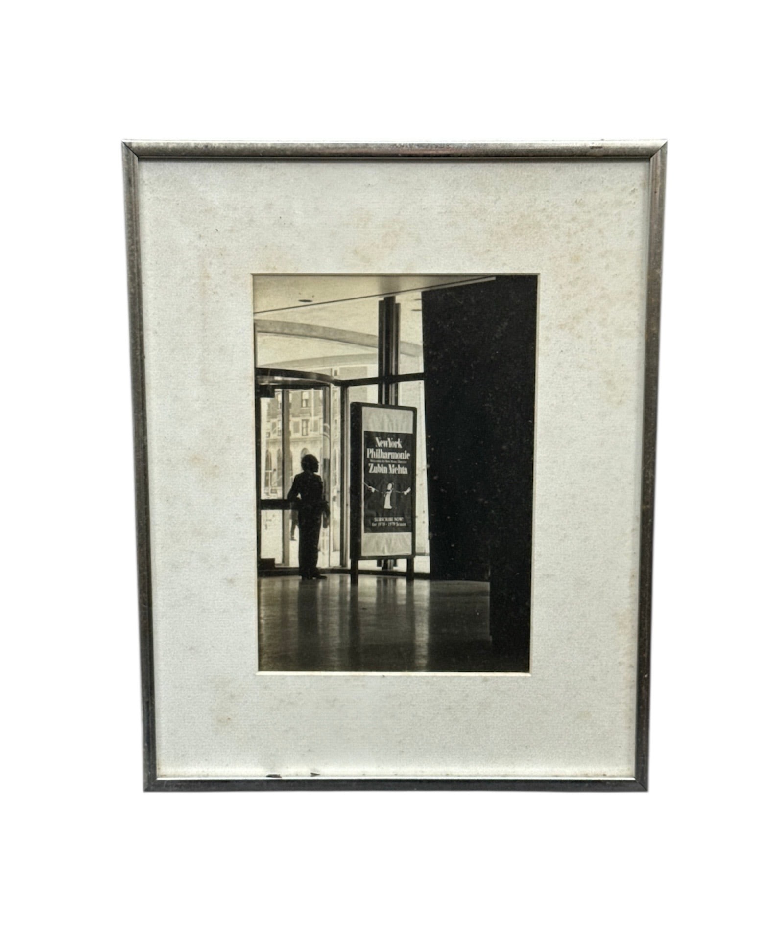 Vintage Black & White Architectural Photograph – Museum Interior Scene: Vintage black-and-white photograph depicting a quiet museum or gallery interior, featuring a solitary figure standing near an exhibition sign within a modern architectural space. The composition highl