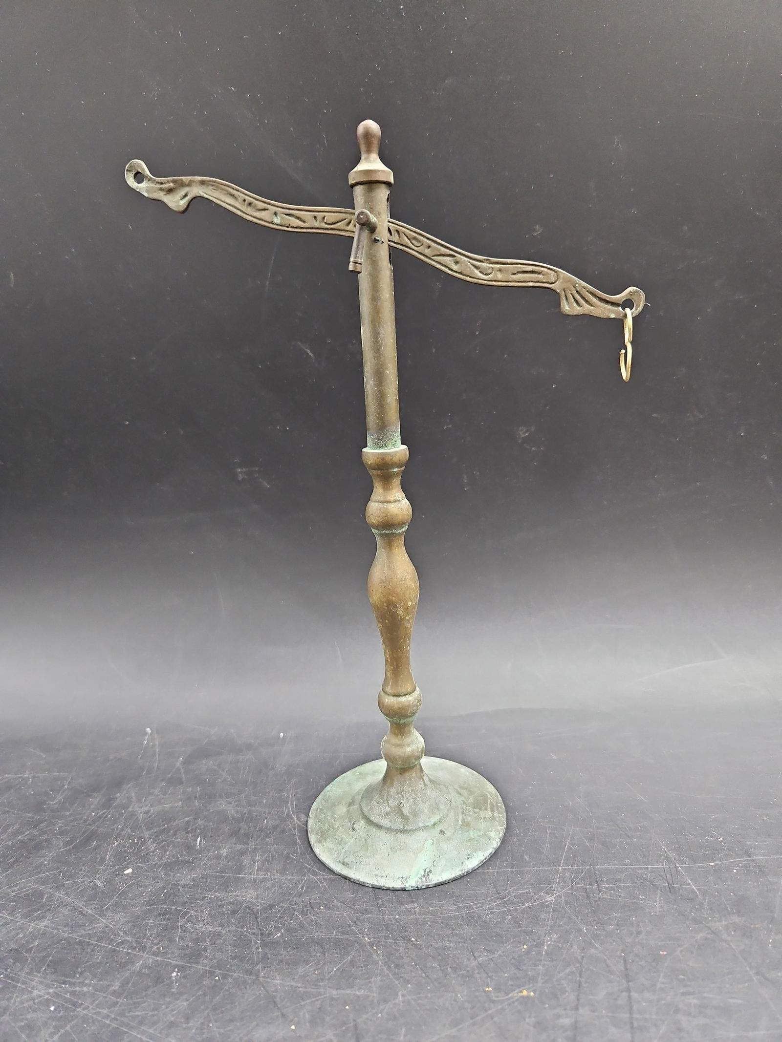 Balance Scale: This antique balance scale features a central turned bronze column with an ornate T-bar arm, designed for hanging scale pans or weights. It is supported by a round, weighted base for stability. This t