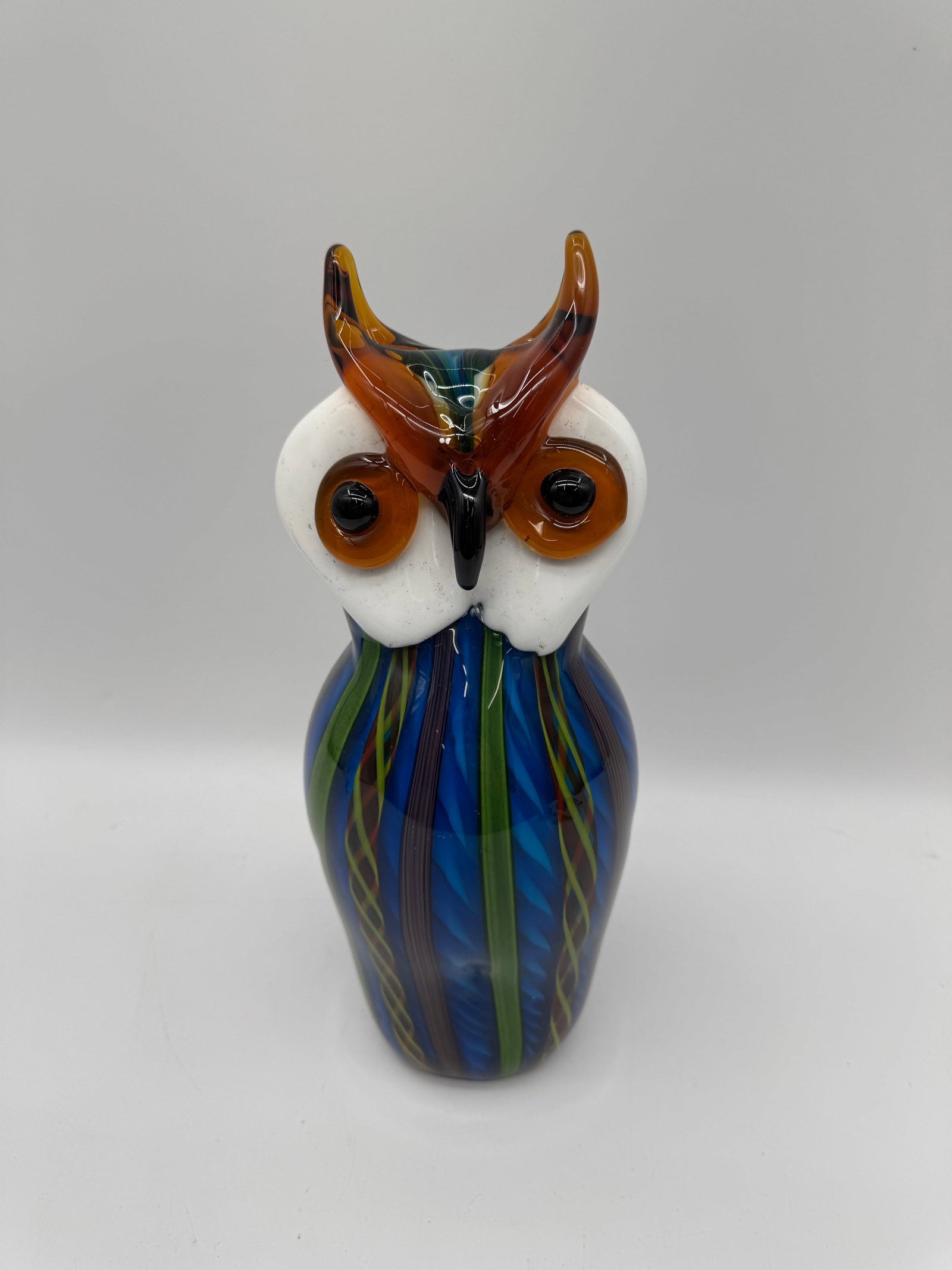 Murano Style Art Glass Owl Figurine: Murano style art glass owl figurine. Features a blue striped body, white head, and amber colored accents. Measures approximately 13 inches tall and 5 inches wide.