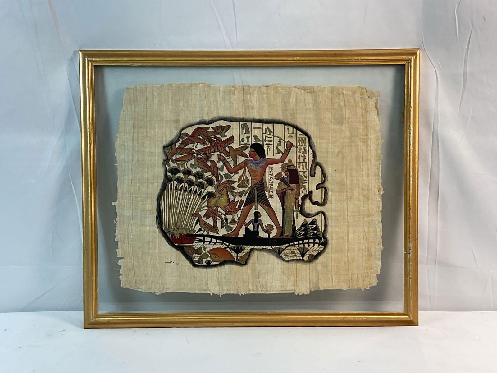 Egyptian Art Papyrus Hunting Scene: Framed Egyptian art papyrus, depicting a hunting scene, hand painted and signed by the artist on the bottom left. Medium: Papyrus tapestry suspended in framed glass Dimensions: H:19in L:23in