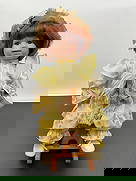 Porcelain Doll on Wooden Rocking Horse: This is a vintage-style porcelain doll with a cheerful expression, dressed in a yellow gingham and floral-patterned dress with puffed sleeves and lace details. The doll has auburn hair styled in a bob