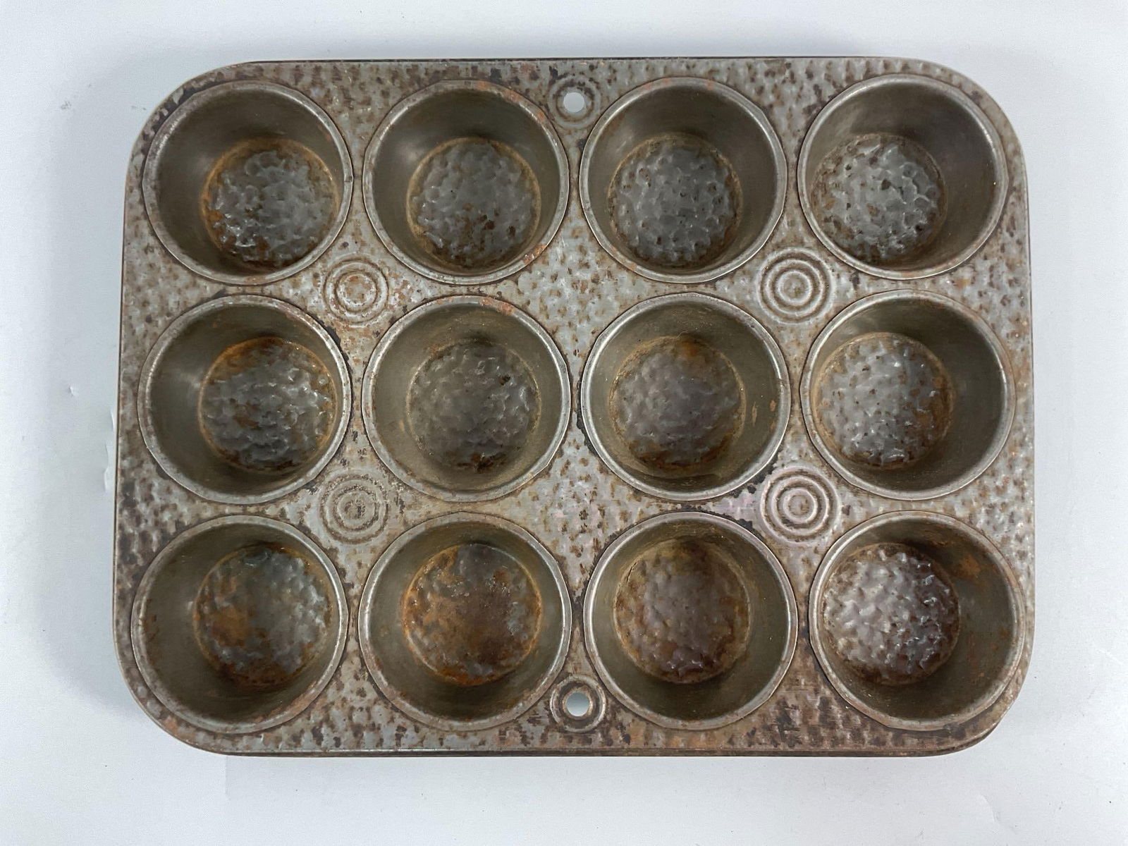 Vintage Hammered Metal Muffin Tin:  A 12-cup vintage muffin or cupcake baking tin with a distinctive hammered metal texture and circular embossing in each cup. Likely made of tin or steel, this piece exhibits signs of age and pati