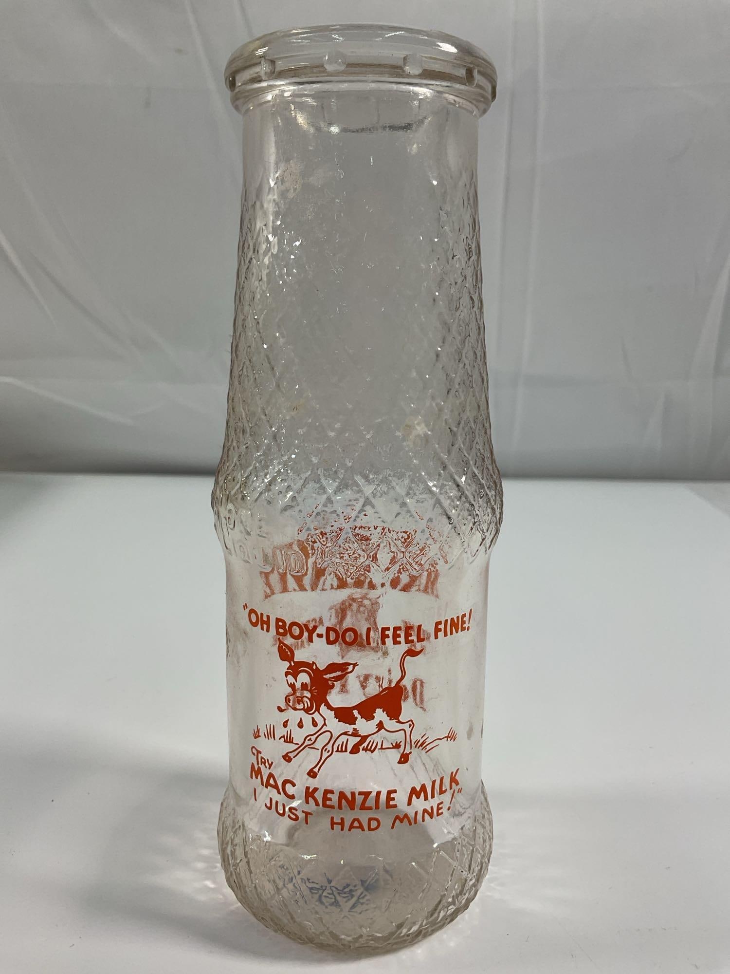 MacKenzie Dairy Farm Milk Bottle - Box 5 - Photo 13: A textured glass dairy bottle from MacKenzie Dairy Farm, featuring orange printed lettering and an illustration of a cow. The bottle’s quilted diamond pattern suggests it was used for cream or