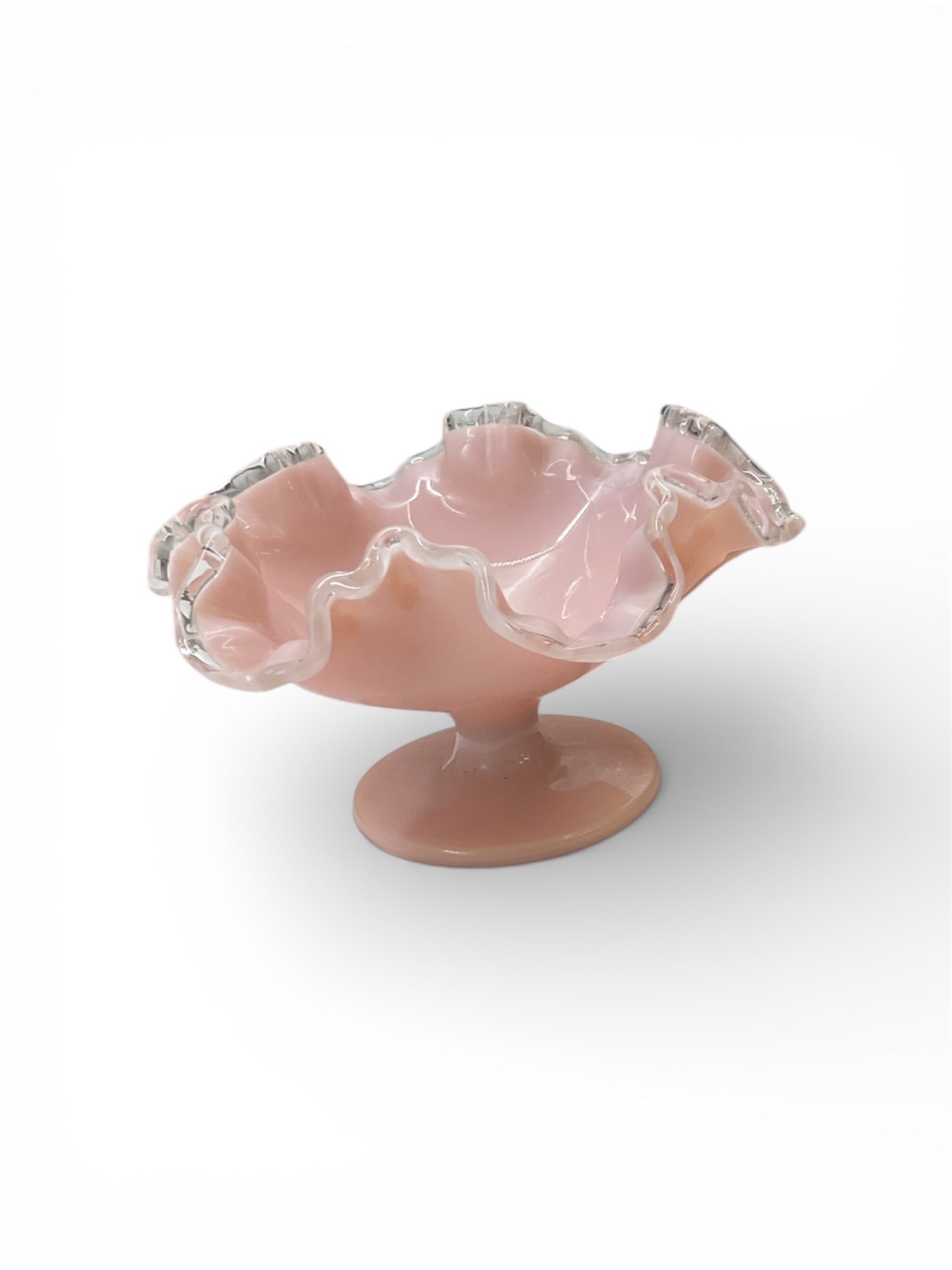 Pink Ruffled Art Glass Compote with Clear Applied Rim: This decorative art glass compote features a softly ruffled bowl form raised on a matching pedestal base. The body displays a warm pink glass tone accented by a clear applied rim that highlights the