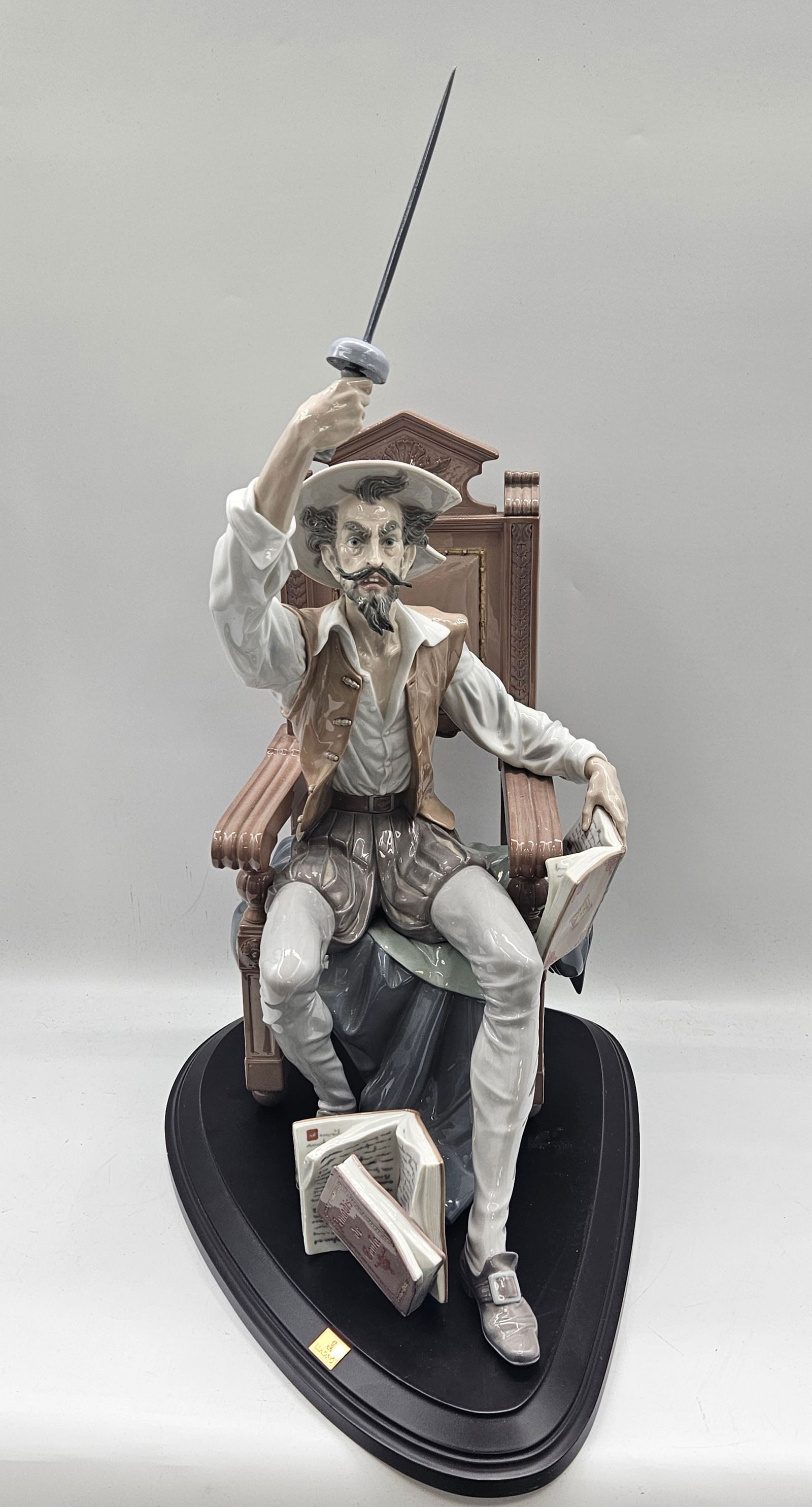 RARE Don Quixote Porcelain Figurine by Lladro: A finely detailed Lladro porcelain sculpture of Don Quixote seated in a dramatic pose, hand raised as if mid-speech. The figure retains excellent detail and coloring, mounted on a custom wooden base.&