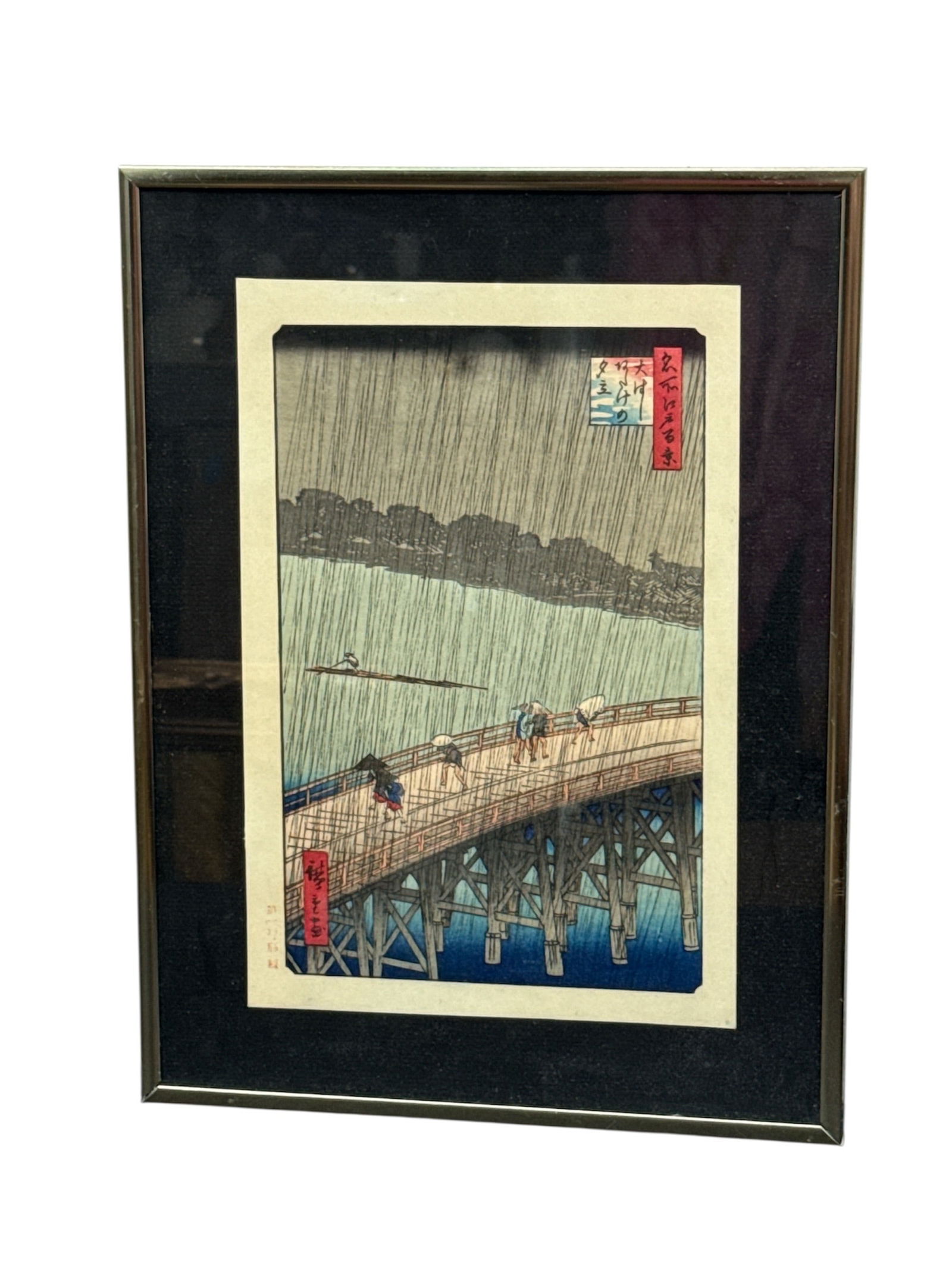 Japanese Woodblock Print of Rain Over Bridge Scene: This framed Japanese woodblock print depicts a dramatic rainy landscape with figures crossing a long wooden bridge over water, rendered in a classic ukiyo-e style. The composition emphasizes vertical