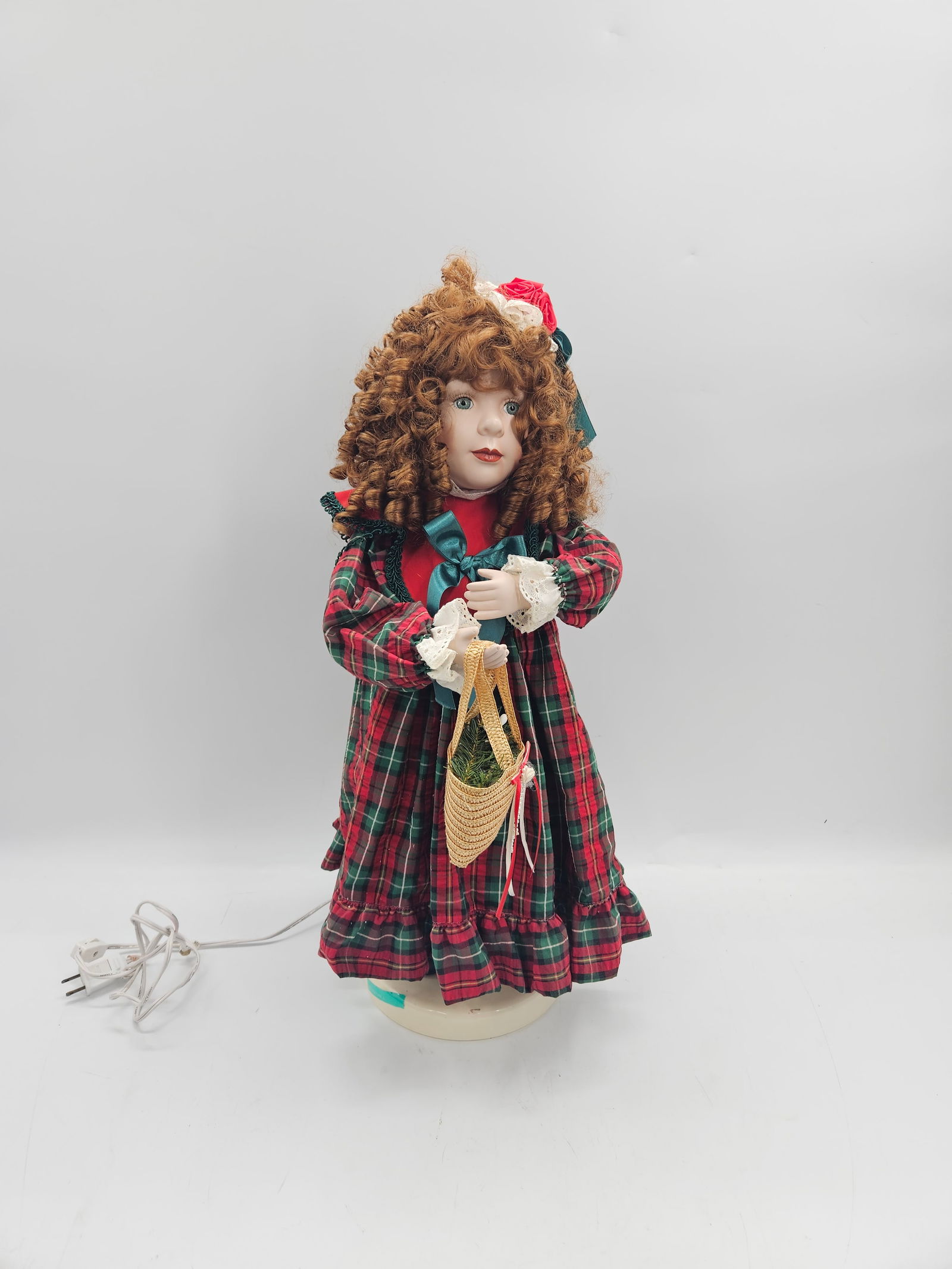 Victorian-Style Porcelain Doll in Holiday Dress: Collectible porcelain doll with curly auburn hair and hand-painted facial features. Dressed in a festive plaid gown accented with lace, ribbon, and a red rose bonnet. The doll holds a small woven bask