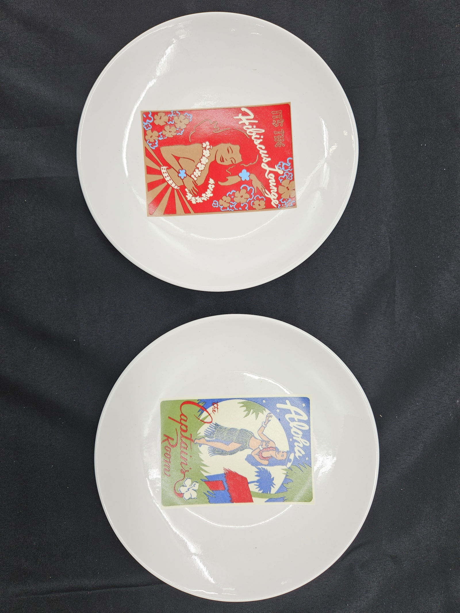 Set of Two Pottery Barn Aloha Girls Recipe Plates: Set of two Pottery Barn Aloha Girls plates. Each plate features a different vintage-style Hawaiian graphic on the front and a cocktail recipe on the back. Each plate is approximately 8 inches in diame