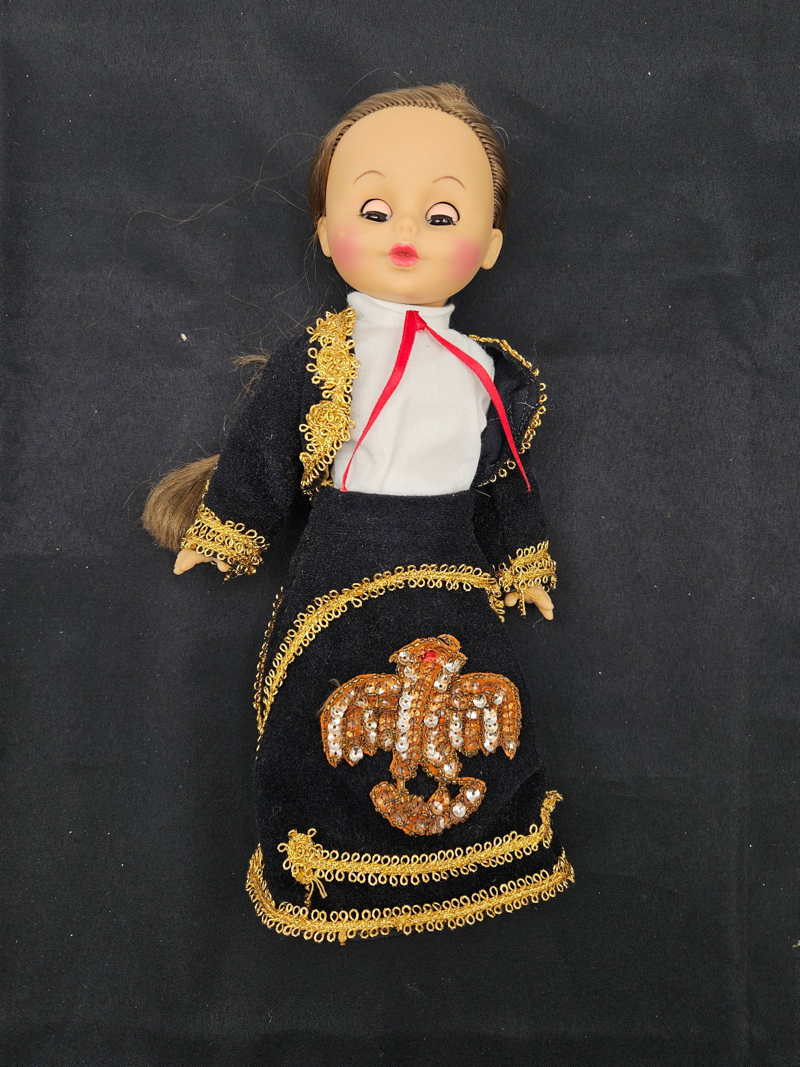 Vintage 12" Matador Doll: Vintage doll, approximately 12 inches tall. Depicts a matador in a black and gold trimmed outfit with an eagle emblem. Features a braided hairstyle. Marked "Uneeda" on the back of the neck.