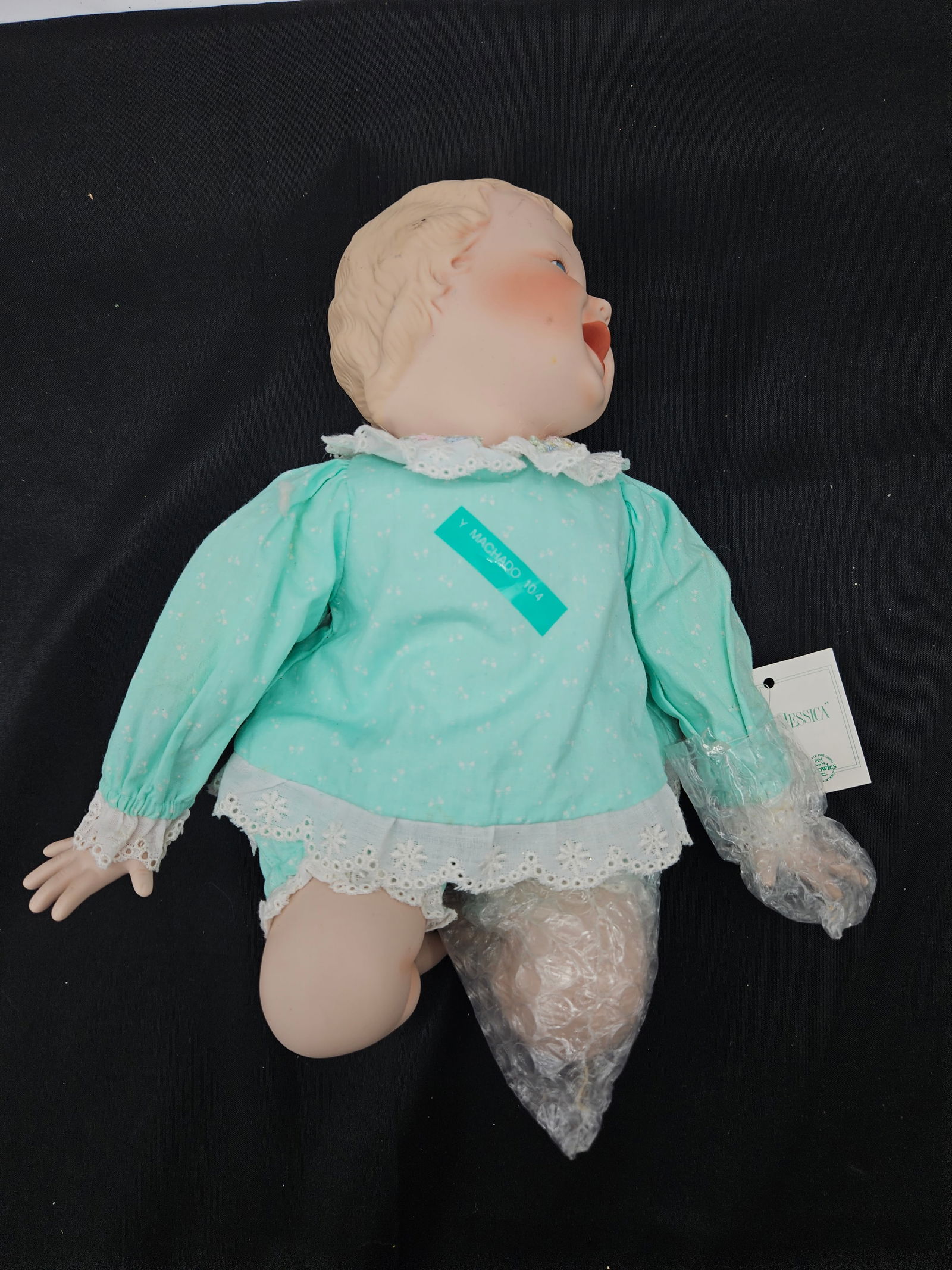 Vintage Porcelain Baby Doll, 11" H: Vintage porcelain baby doll with painted features and light blue clothing with lace trim. Measures approximately 11 inches in height and 10 inches in width at its widest point. Some parts are wrapped