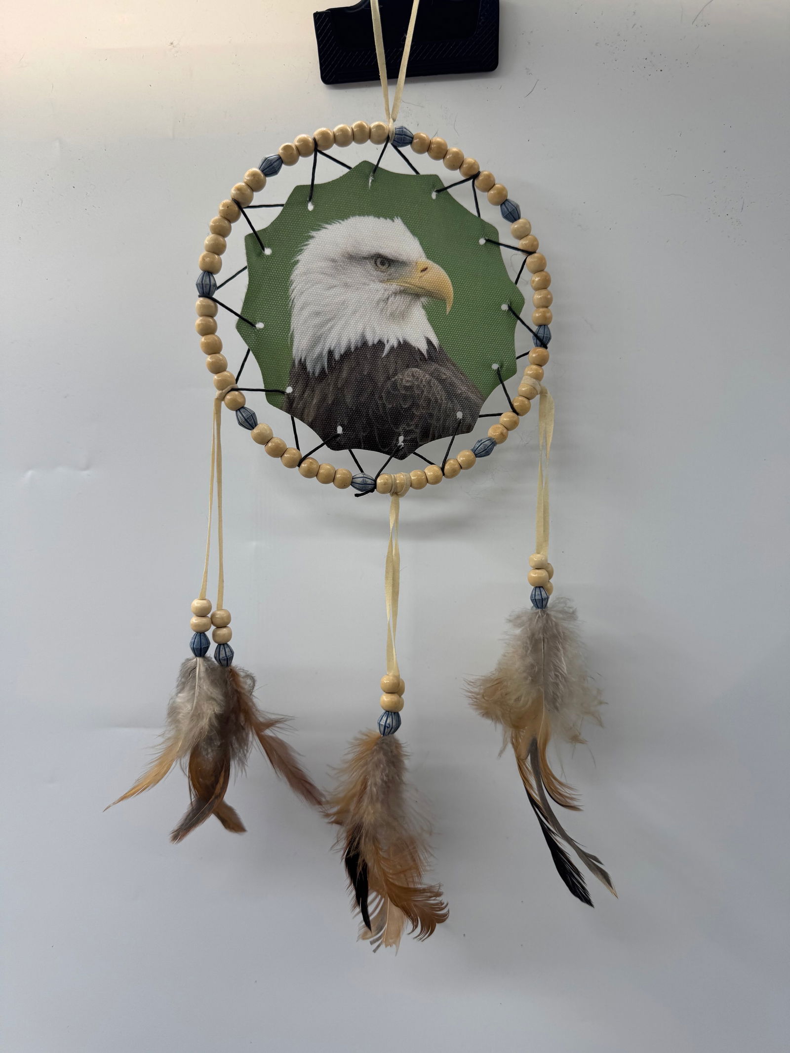 Eagle Dreamcatcher: Handmade dreamcatcher featuring an eagle image, wooden beads, and feathers. Measures approximately 15 x 6 inches.