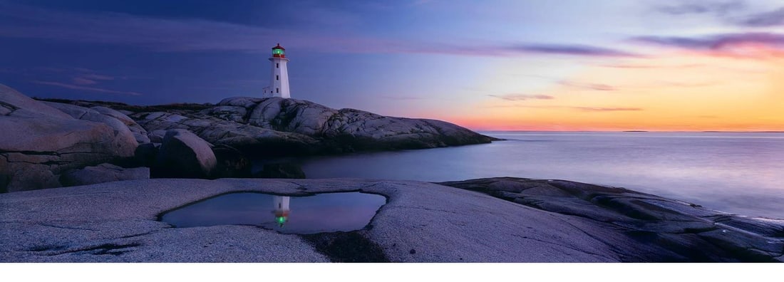 Atlantic Reflection by Peter Lik (Australian, b.1959): Striking panoramic photograph by world-renowned landscape photographer Peter Lik, capturing a tranquil coastal scene at sunset. A solitary lighthouse stands on rugged rocks, its reflection perfectly m