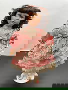 Porcelain Doll in Pink Satin and Lace Dress: This elegant porcelain doll features dark curly hair and a gentle, expressive face. She is dressed in a soft pink satin dress accented with detailed ivory lace overlay and a large matching bow at the