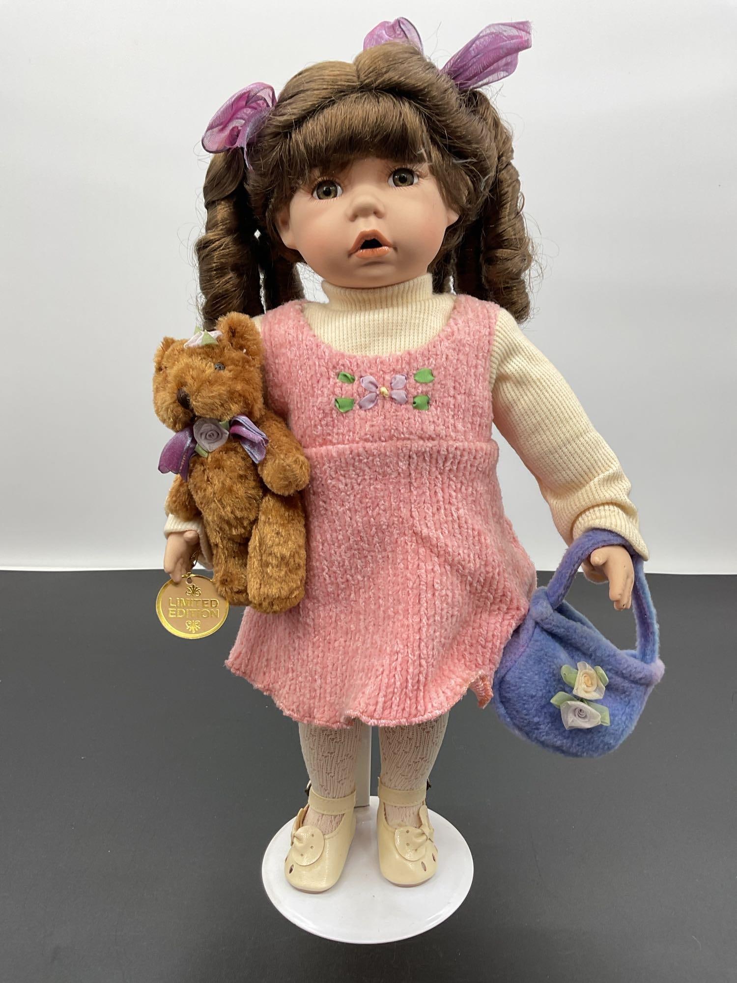 Porcelain Doll with Teddy Bear and Purse - DanDee: This expressive porcelain doll features brown curly pigtails tied with purple ribbons and an open-mouth surprised expression. She wears a pink knit jumper with floral embroidery over a cream-colored l