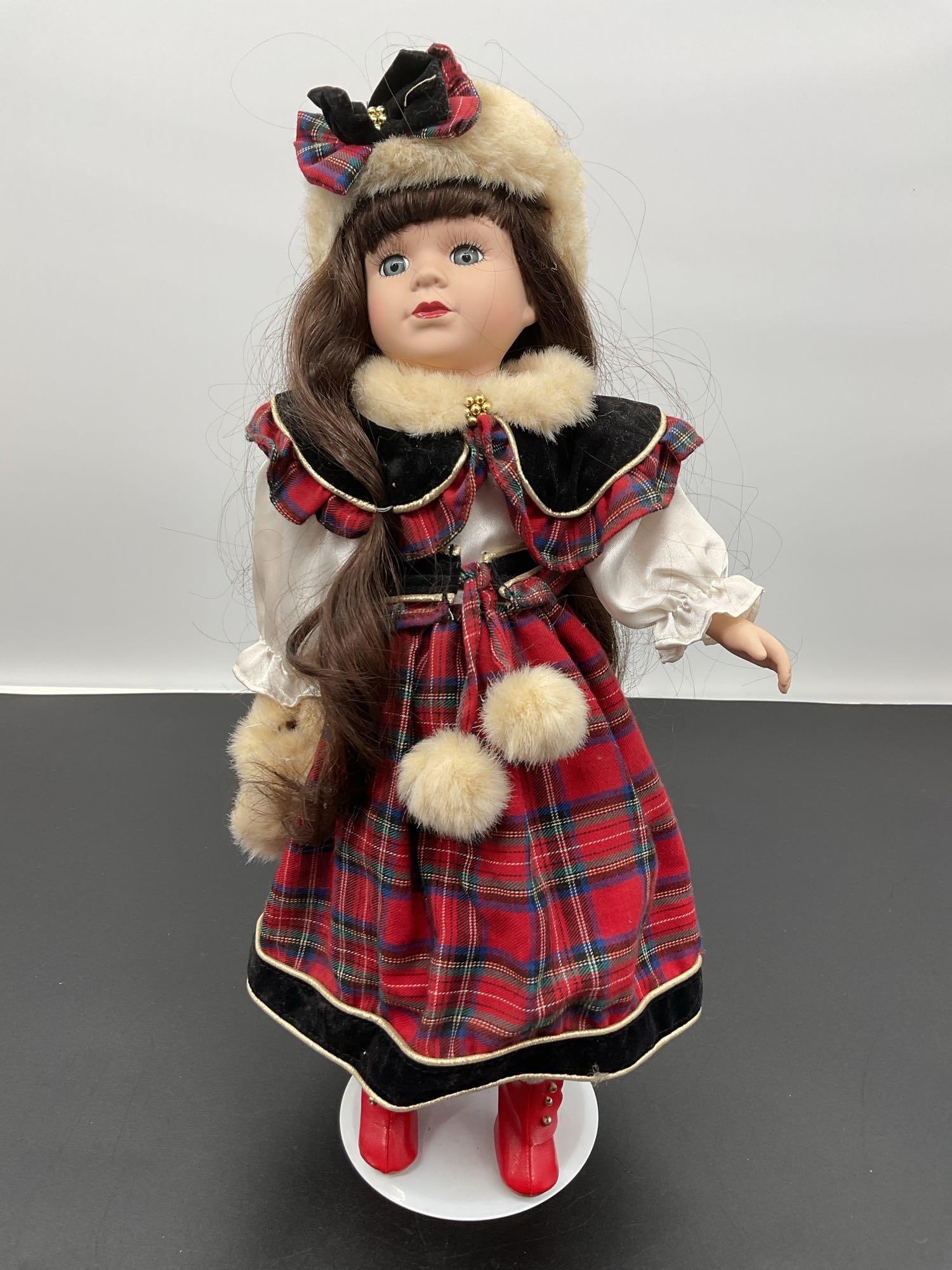 Porcelain Doll in Holiday Plaid Outfit: This porcelain doll features long brown hair, blue eyes, and a gentle expression. She is dressed in a festive holiday-themed outfit with a red and green tartan plaid skirt, white blouse with puffed sl