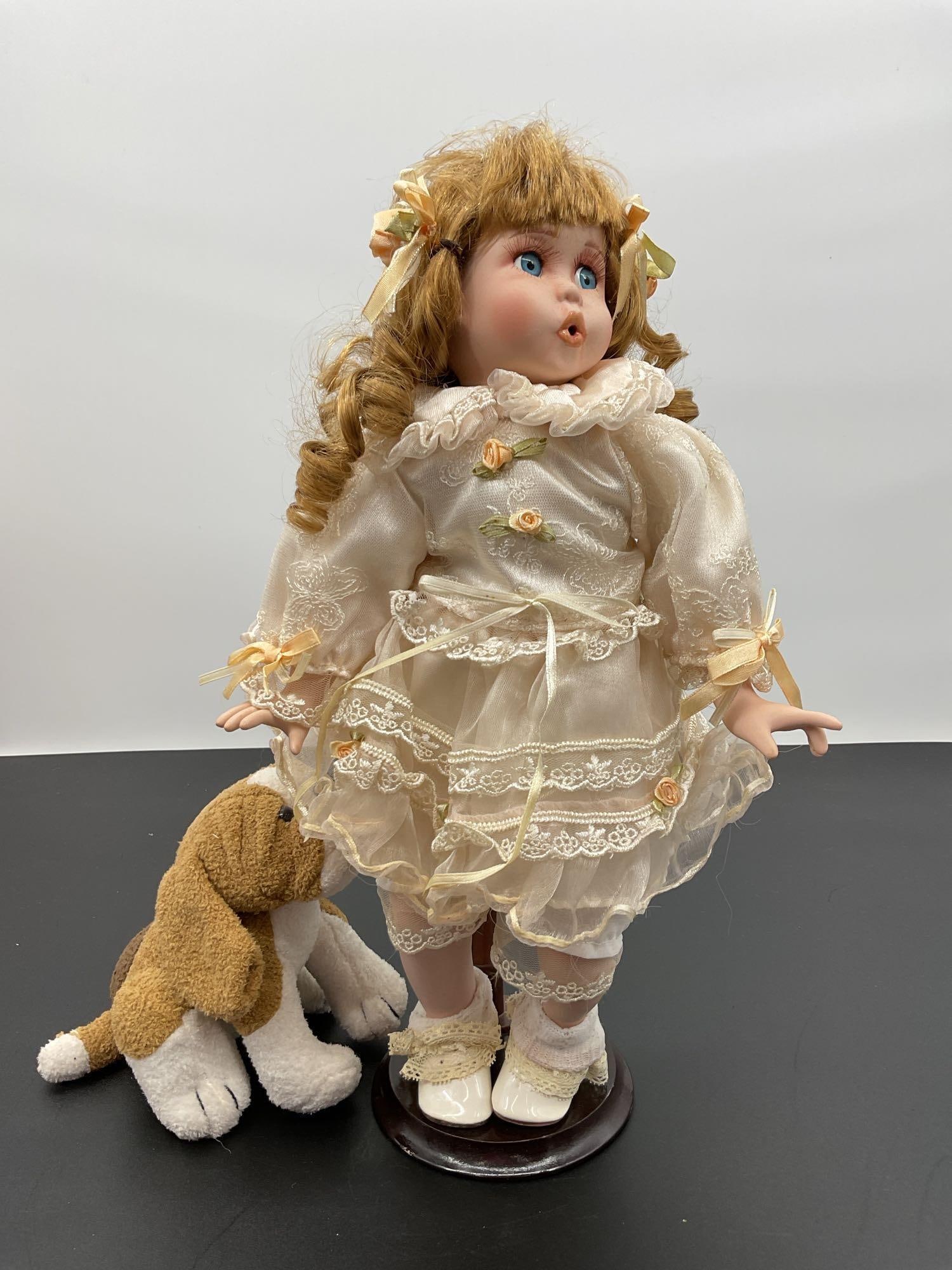 Porcelain Doll in Cream Lace Dress with Stuffed Dog: This expressive porcelain doll features curly golden hair tied with peach ribbon bows and bright blue eyes looking upward with a surprised or singing expression. She wears a vintage cream lace dress w