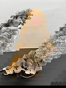 Porcelain Doll in Cream Lace Dress with Stuffed Dog: This expressive porcelain doll features curly golden hair tied with peach ribbon bows and bright blue eyes looking upward with a surprised or singing expression. She wears a vintage cream lace dress w