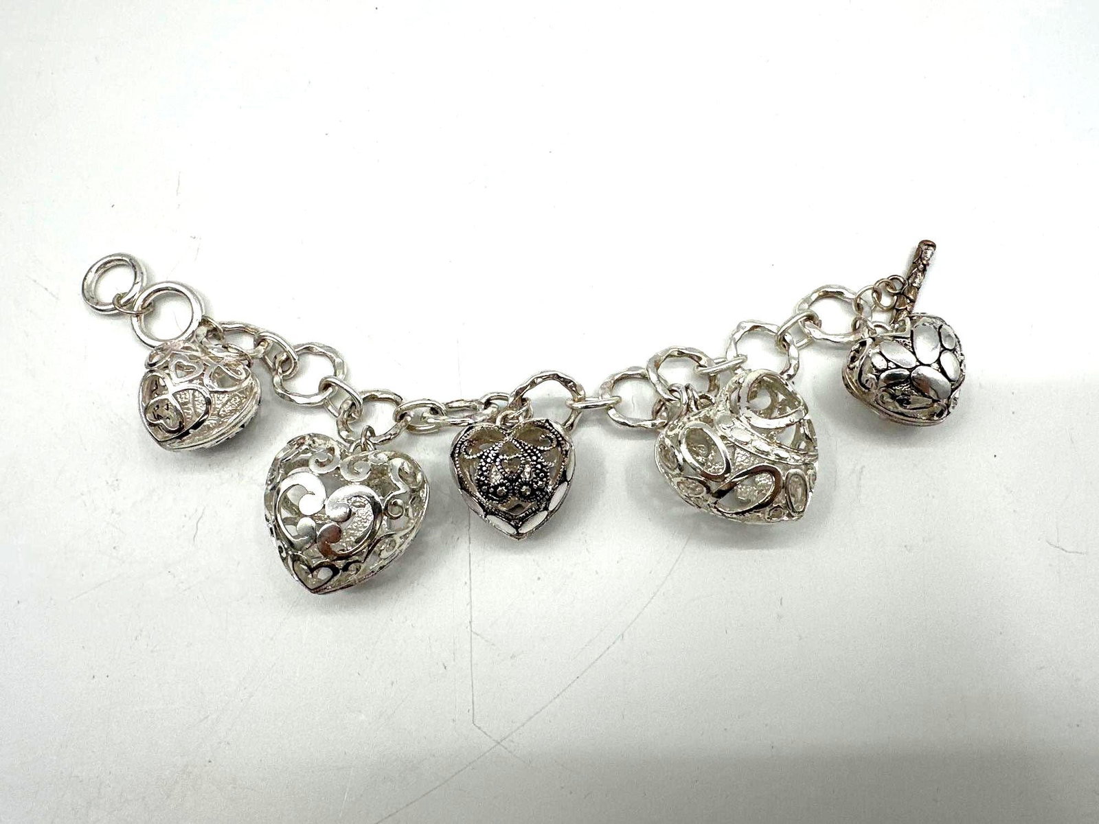 Silver-Tone Filigree Heart Charm Bracelet: Eye-catching charm bracelet featuring five large, hollow filigree heart charms attached to a chunky silver-tone chain. Each heart showcases intricate scrollwork designs. Secured with a toggle clasp,