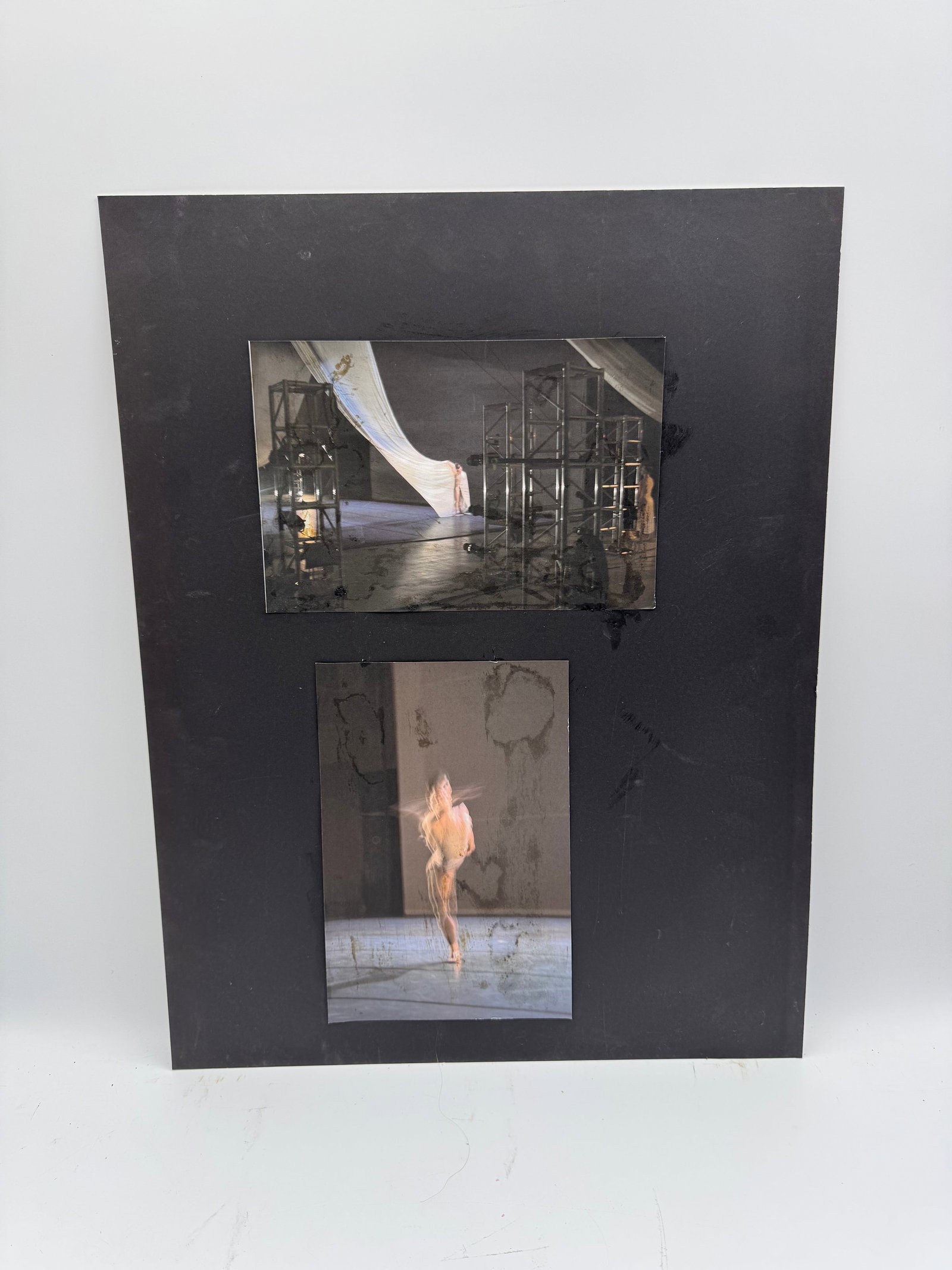 Dance Performance Photographs: Mounted display featuring two color photographs of a stage performance. The top image shows a theatrical set with draped fabric and scaffolding, while the lower image captures a blurred motion shot