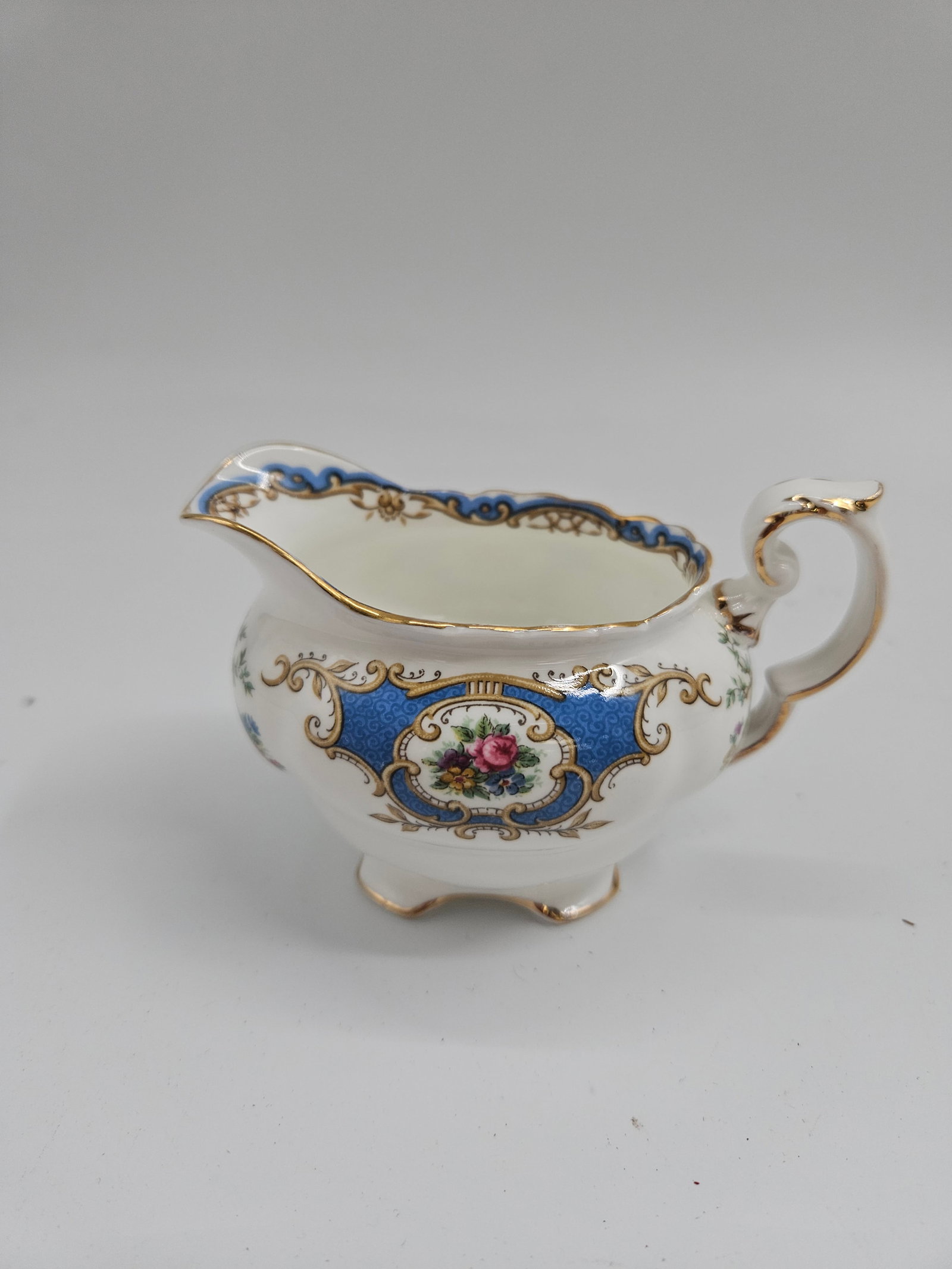 Coalport Porcelain Creamer: Elegant vintage Coalport porcelain creamer featuring a cobalt blue band with floral medallion and gold gilt accents. Scalloped edge and ornate handle design. Dimensions: H:3 in W:2 in L:4