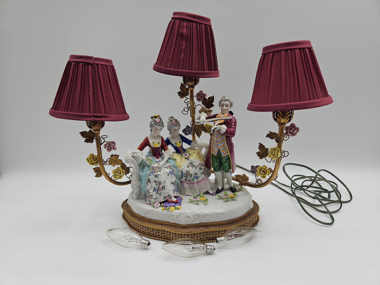 Dresden Figural Lamp with Three Shades: Dresden figural lamp featuring a central porcelain group of figures in 18th-century dress. The lamp has three arms with shades. Approx Dimensions: 19 in length from outer shade to outer shade 8
