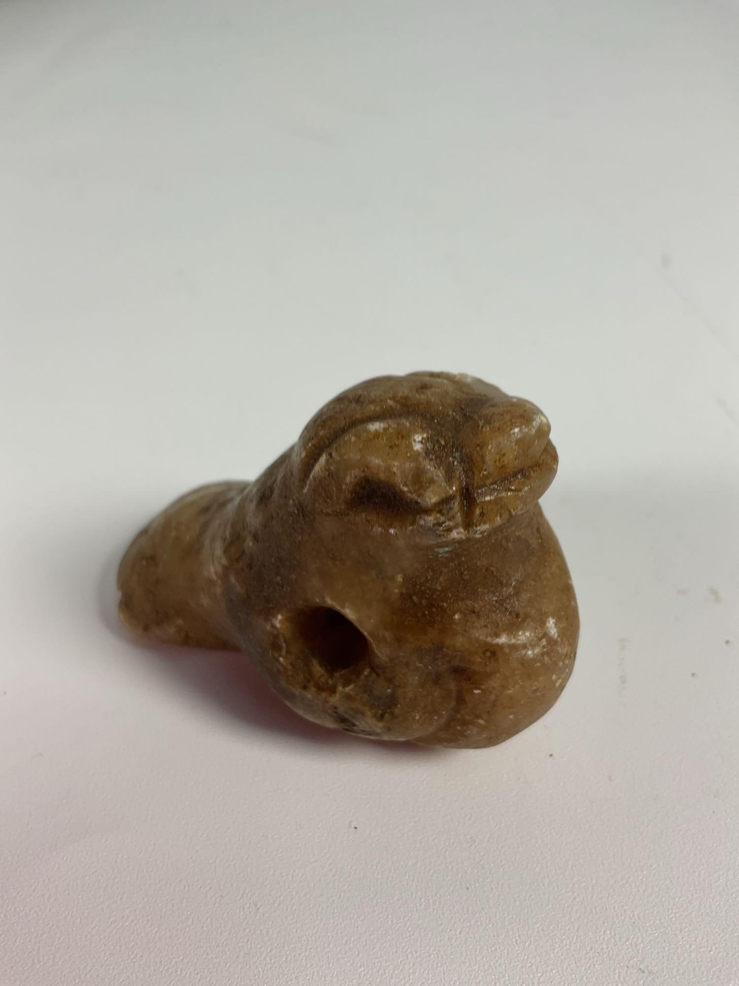 Pre-Columbian Carved Stone Amulet – Zoomorphic or Anthropomorphic Form: A small, brownish carved stone artifact featuring a hole, possibly for suspension as an amulet or pendant. The shape resembles an abstract or zoomorphic figure, potentially representing an animal or