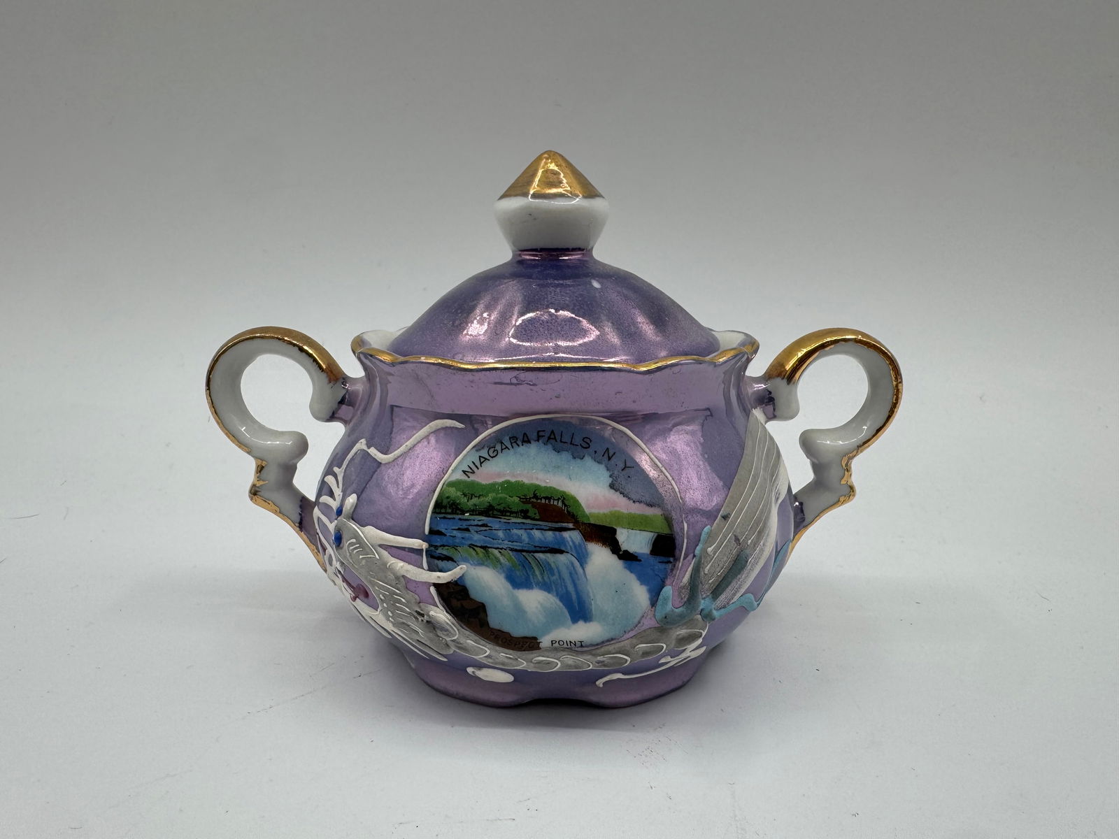 Vintage Japanese Niagara Falls Souvenir Sugar Bowl: Vintage Japanese sugar bowl with lid. Features a lavender iridescent finish, gold accents, and a Niagara Falls scene. Marked 'Made in Japan' on the base. Dimensions: 4" H x 6" W x