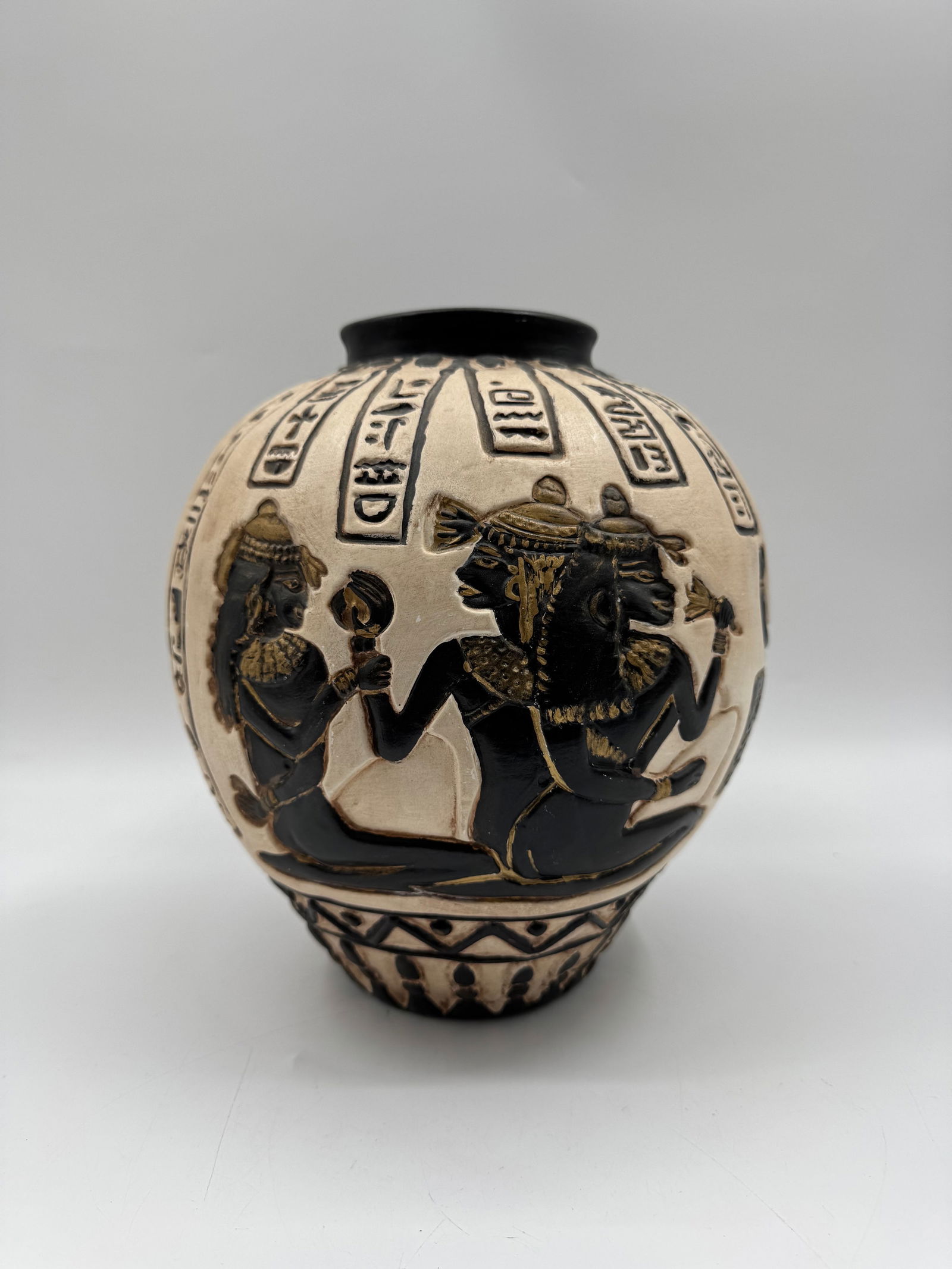 Egyptian Style Relief Carved Ceramic Vase: Ceramic vase with Egyptian-style relief carvings of figures and hieroglyphs. Black and beige coloration. Dimensions: H 11 in, D 10 in.