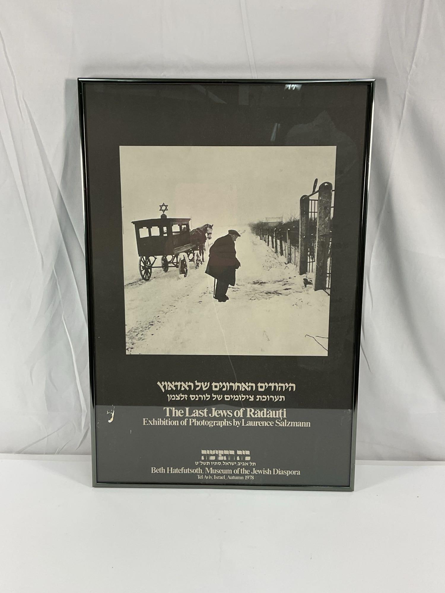 The Last Jews of Radauti: A framed exhibition poster featuring a black-and-white photograph from The Last Jews of Radauti by Laurence Salzmann. The image captures a historical moment in a snowy setting, with a figure walking b