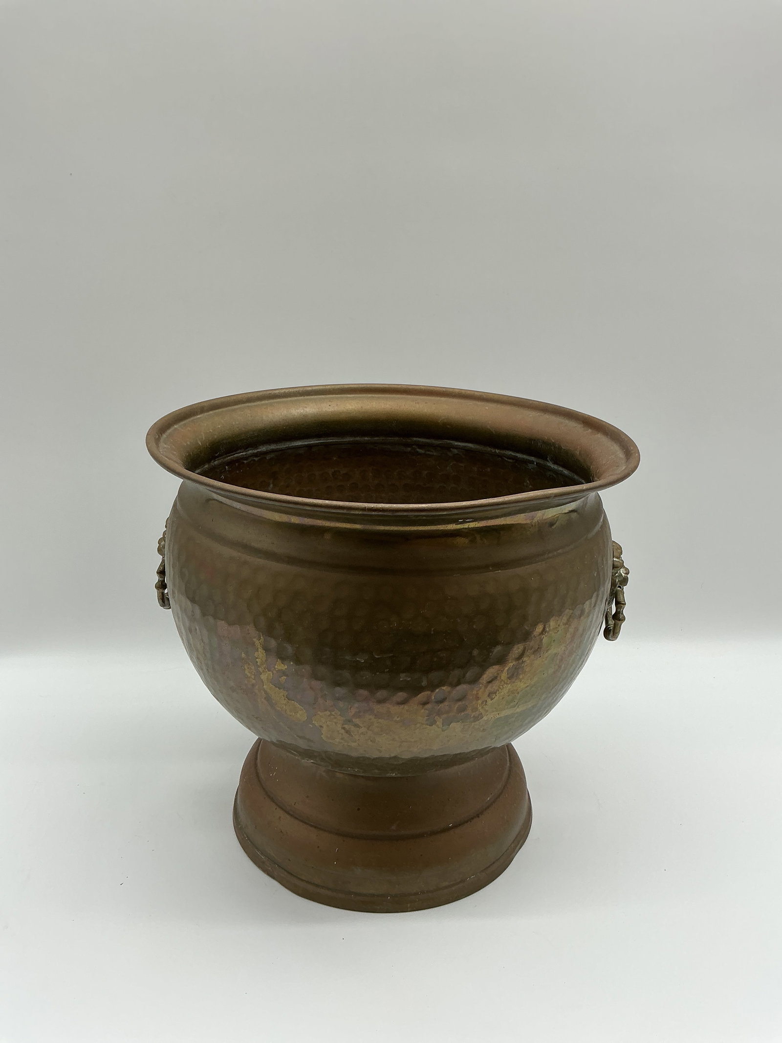 Hammered Copper Pedestal Bowl with Lion Head Decoration: Hammered copper pedestal bowl with applied lion head decoration. The bowl features a flared rim and a decorative pedestal base. A unique and decorative piece. approx 12 in W x 11 in H