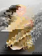 Porcelain Angel Doll in Ivory and Gold with Feather Wings: This porcelain angel doll features long auburn hair and soft blue eyes with a serene expression. She is dressed in an elaborate ivory gown with pleated and lace fabric, adorned with gold ribbon and me